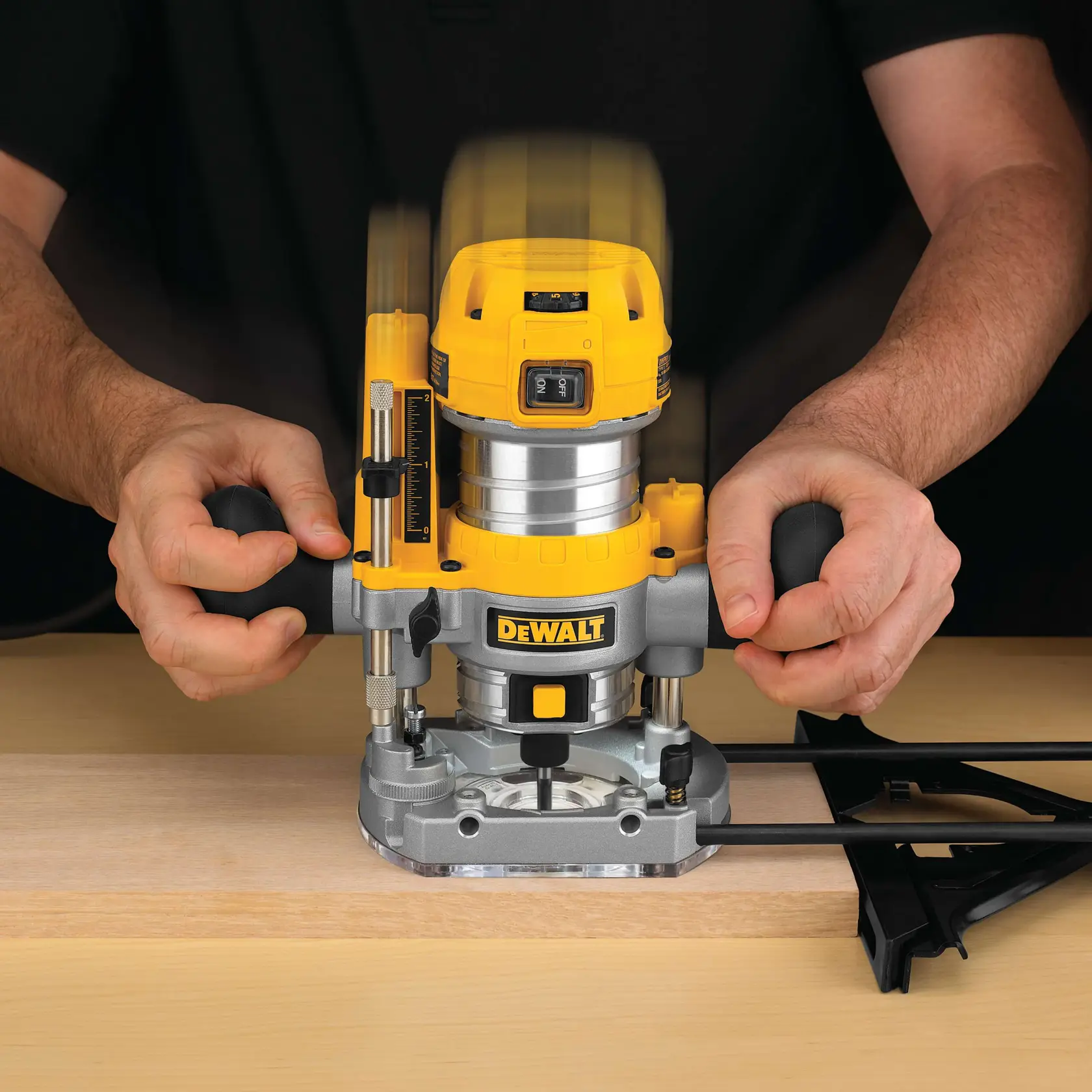Nahaufnahme einer Person, die einen DEWALT D26203 Oberfräse auf einem Holzstück benutzt, wobei beide Hände die Griffe halten und das Gerät in Betrieb ist.