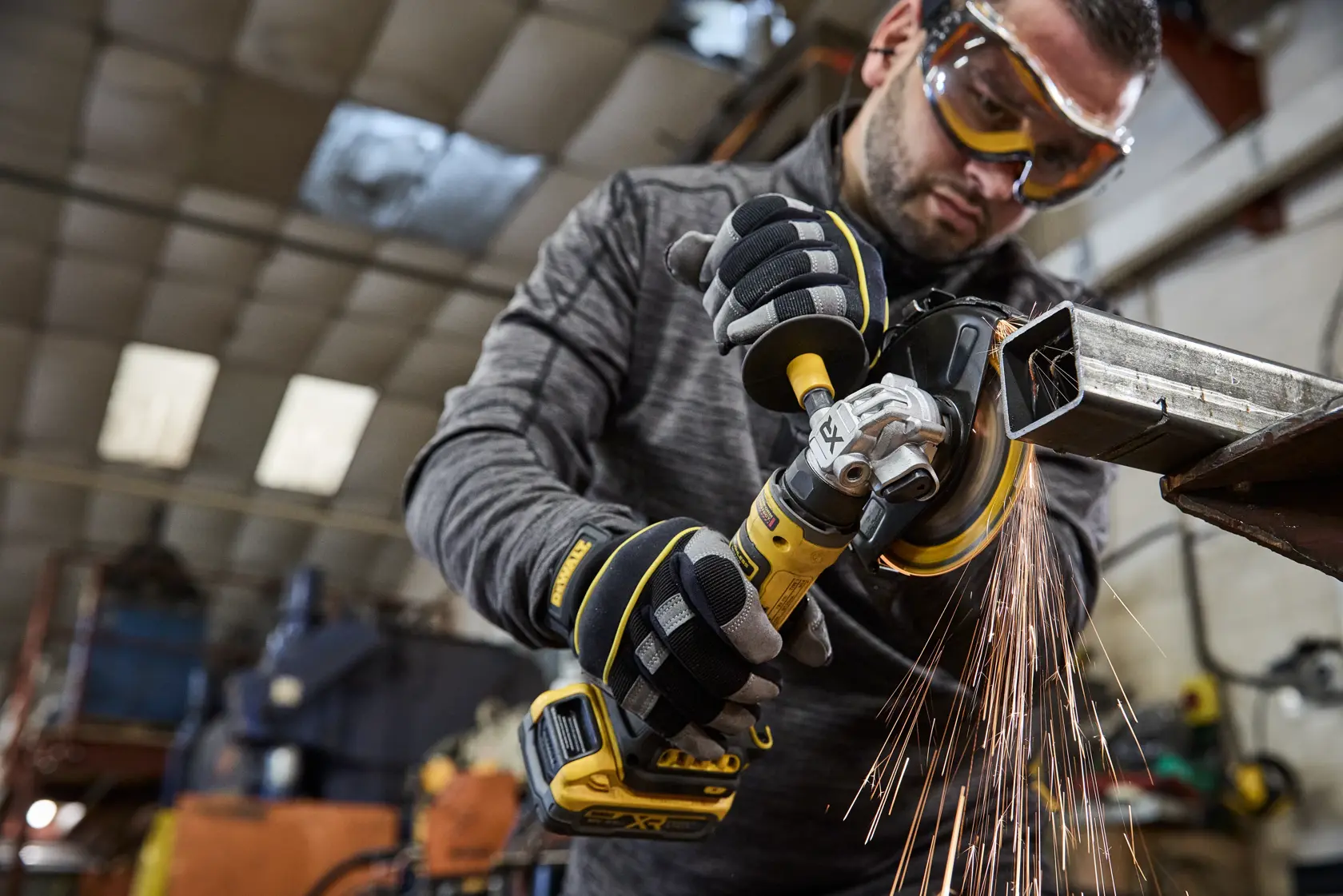 Person nutzt einen DEWALT Akku-Winkelschleifer am Metall mit Funken in einer Werkstatt.