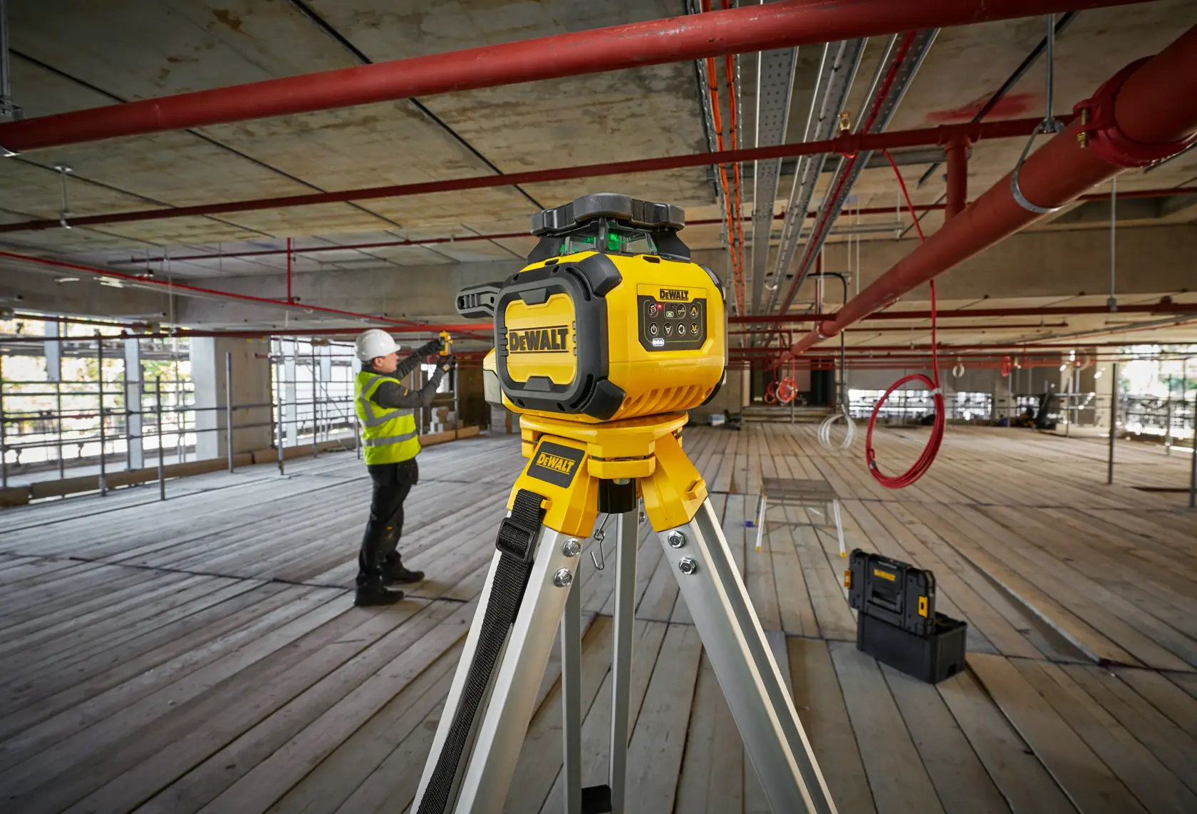 DEWALT DCLE15221G-QW, DCLE15221G Foto-Werkzeug auf Stativ, Baustelle. Arbeiter und Werkzeugkiste im Hintergrund.