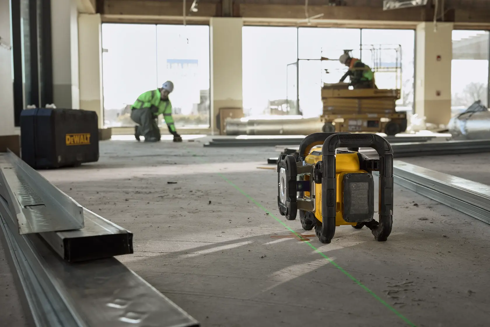 Gelber DEWALT-Laser auf Baustellenboden, mit Arbeitern und Baumaterial im Hintergrund.