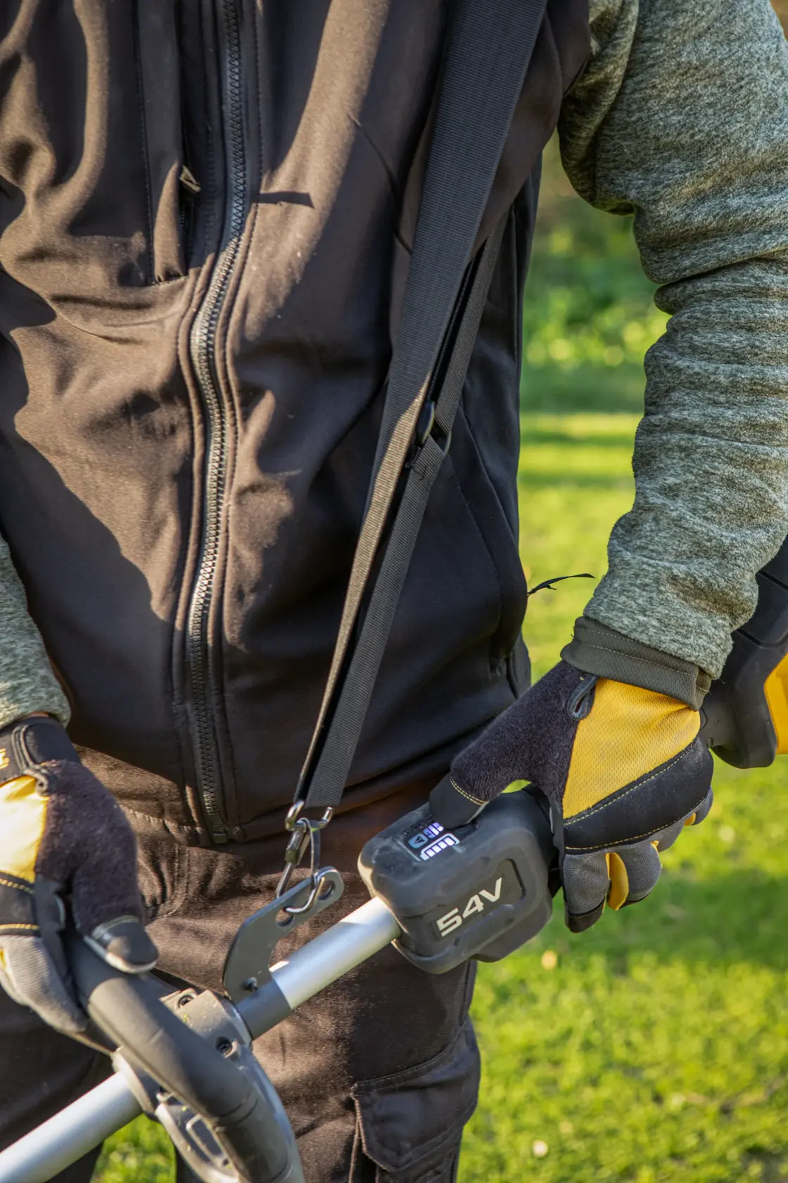 Person mit Handschuhen hält DEWALT 54V Gartengerät draußen und trägt eine Jacke mit Reißverschluss.