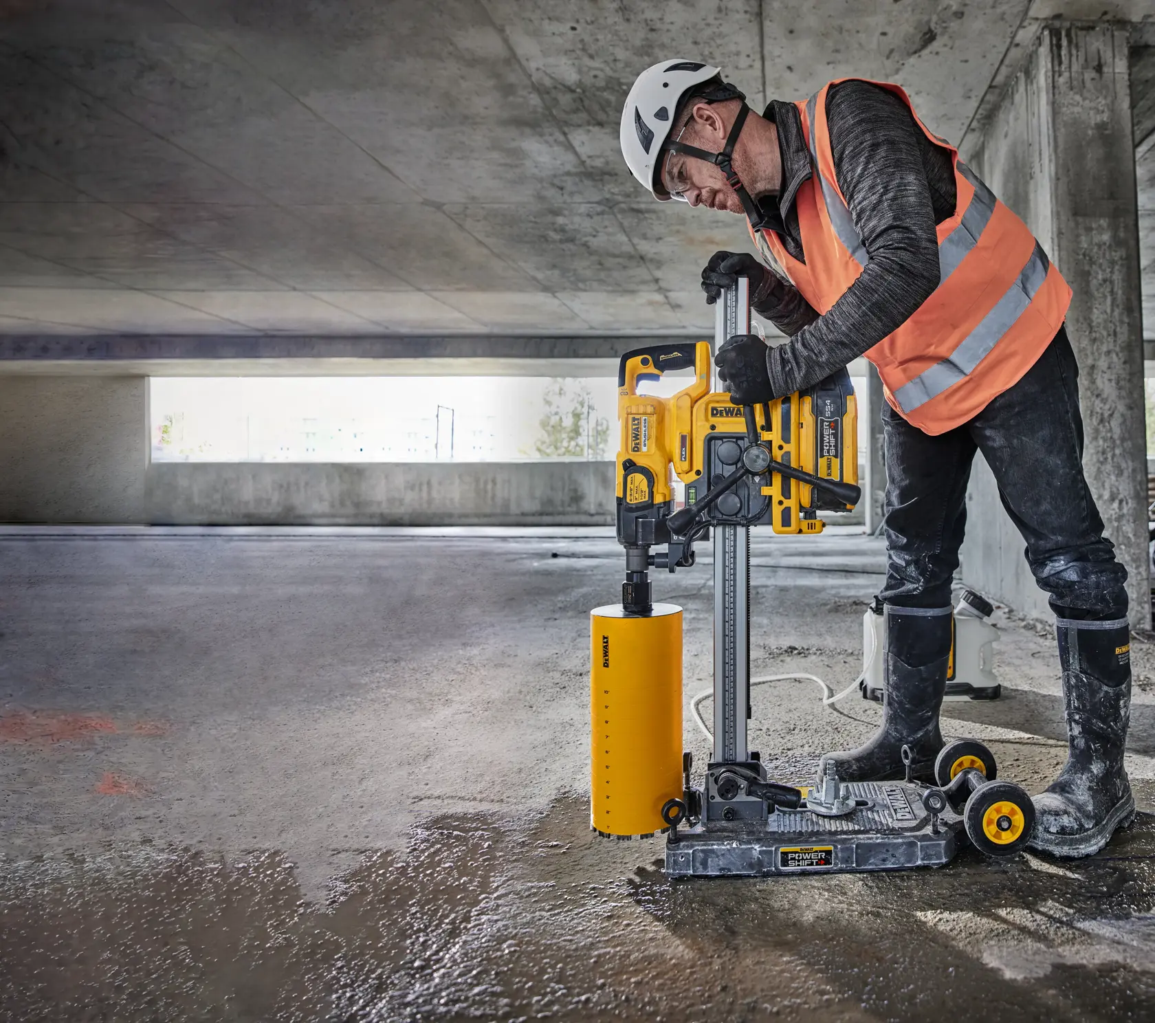 Trabajador usa perforadora DEWALT DCPS151 en concreto húmedo de un estacionamiento, con equipo de seguridad.