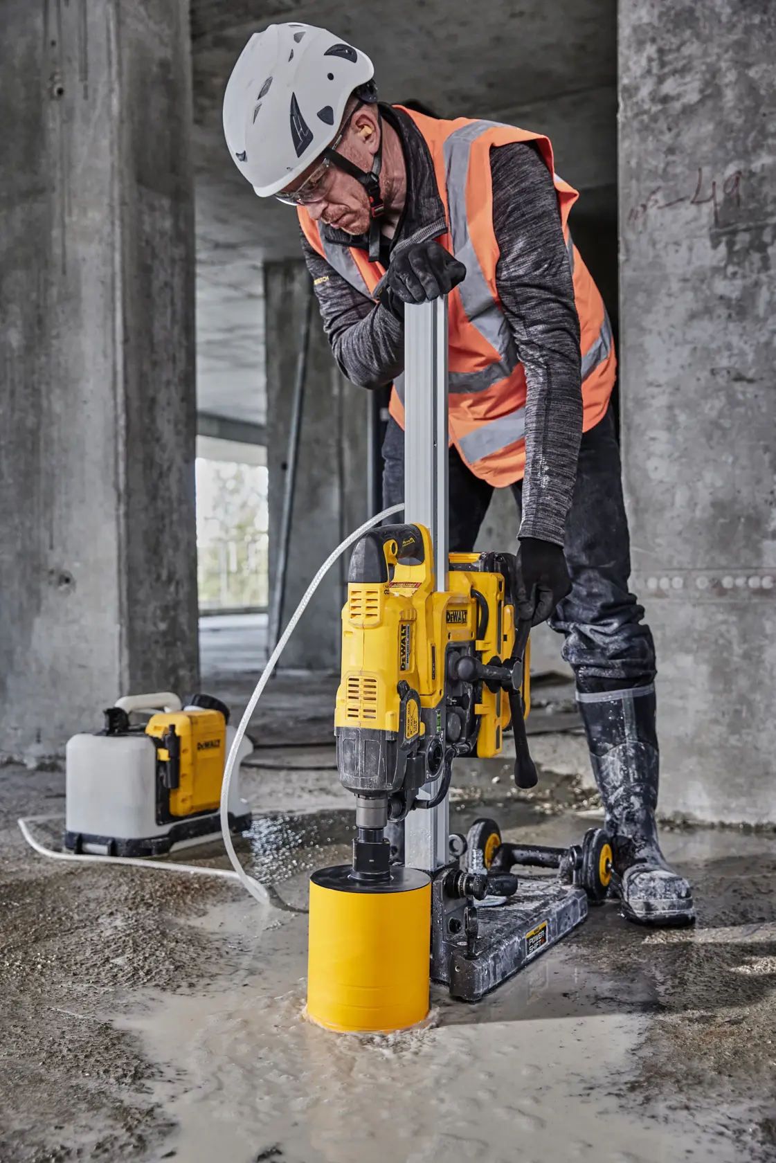 Trabajador usa taladro DEWALT DCPS151 sobre suelo de concreto mojado en una obra en construcción.