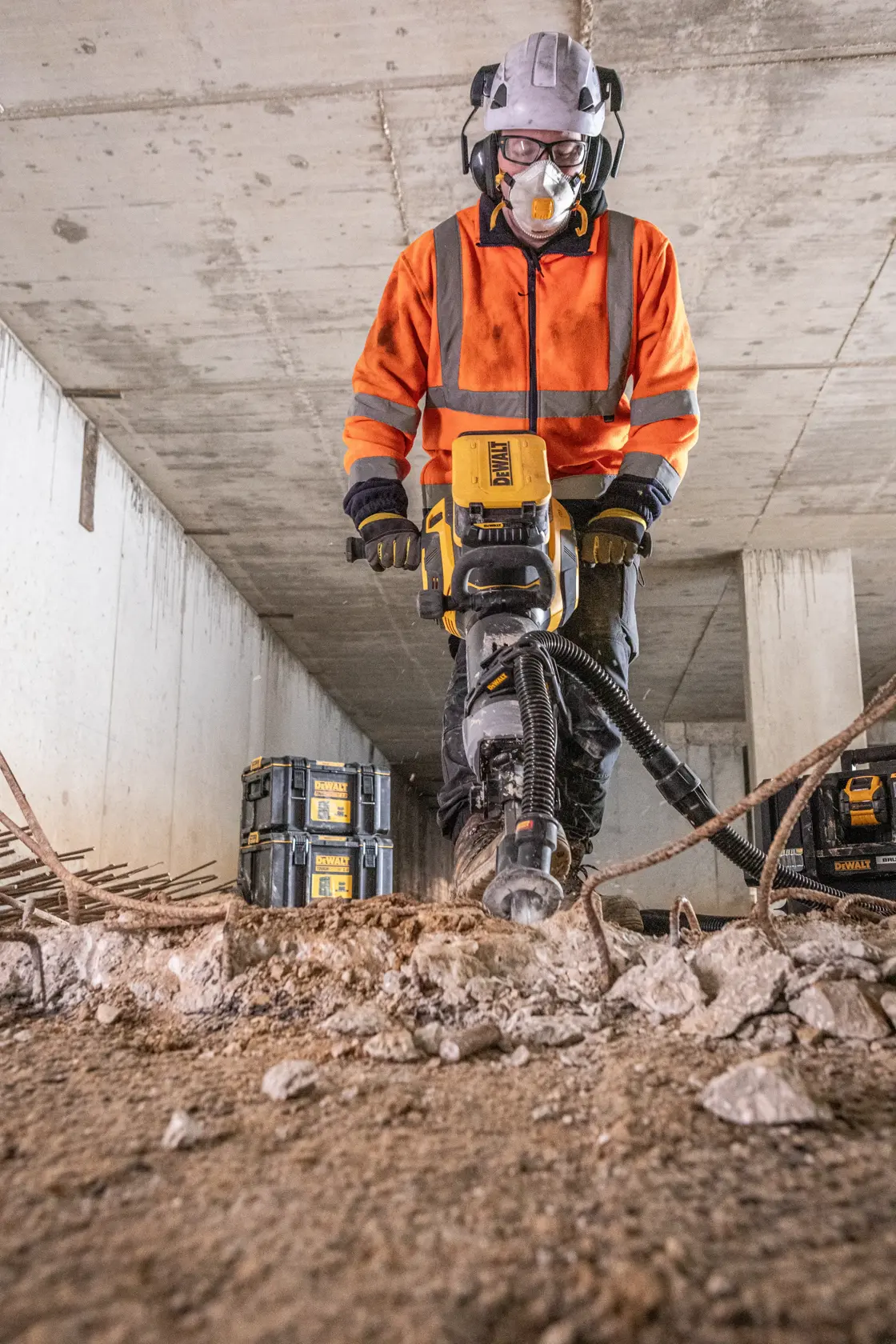 Arbeiter nutzt DEWALT DCPS966N Abbruchhammer, sichtbare Sicherheitsausrüstung und Werkzeugboxen.