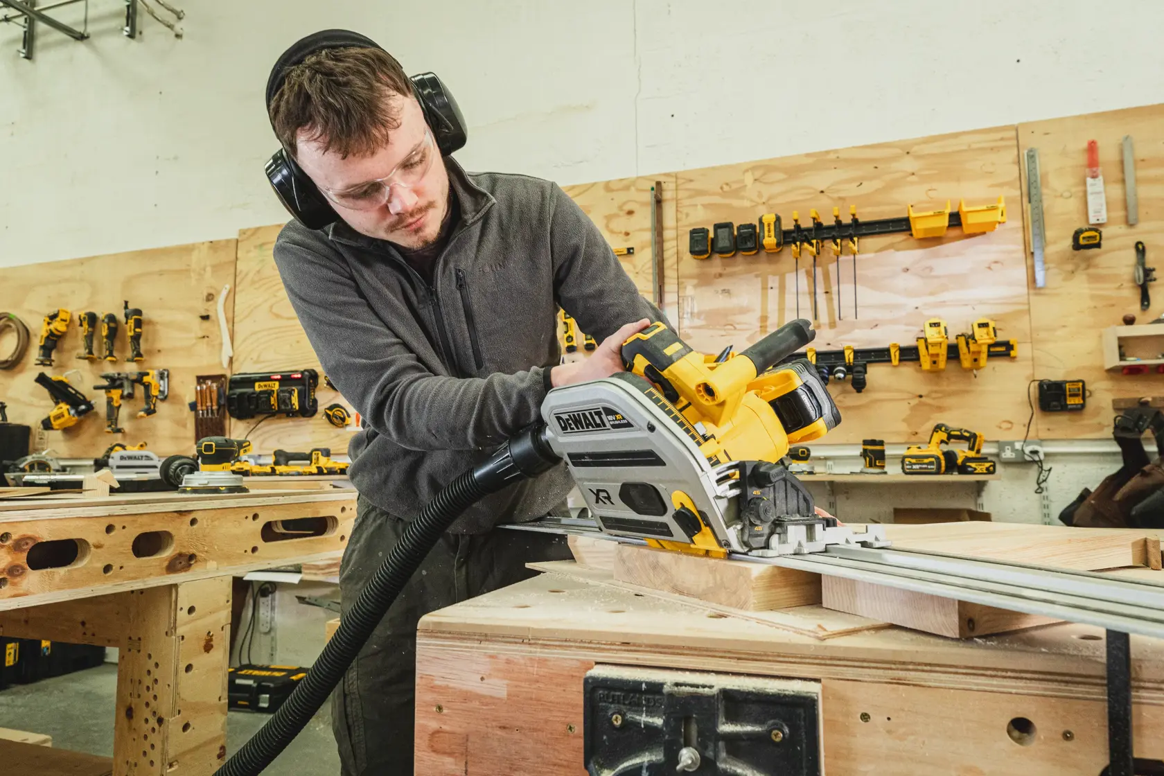 Person nutzt eine DEWALT Akku-Tauchsäge im Holzwerkstatt, mit Gehör- und Augenschutz.