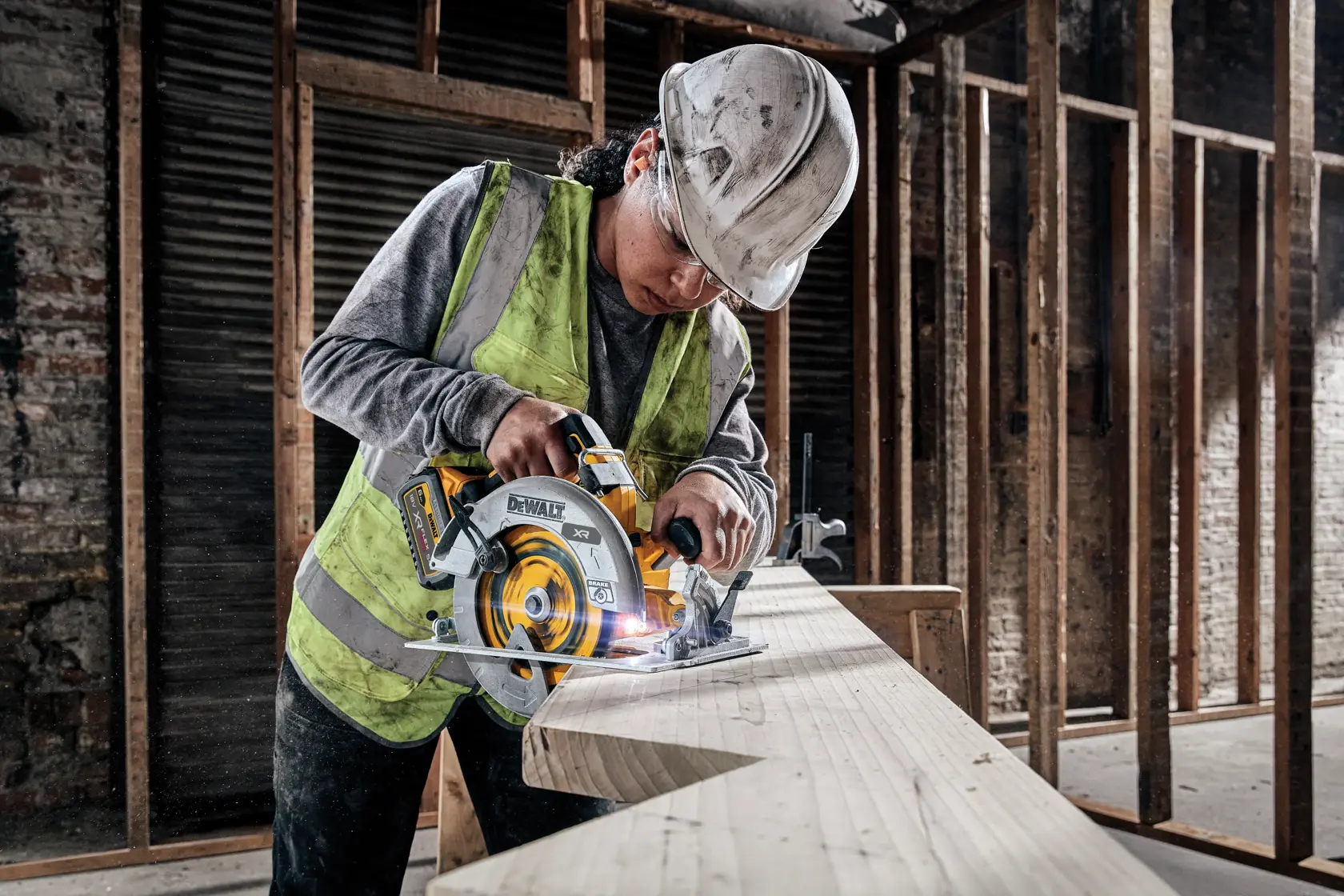 Trabajador corta madera con sierra circular DEWALT en obra. Lleva chaleco y casco de seguridad.
