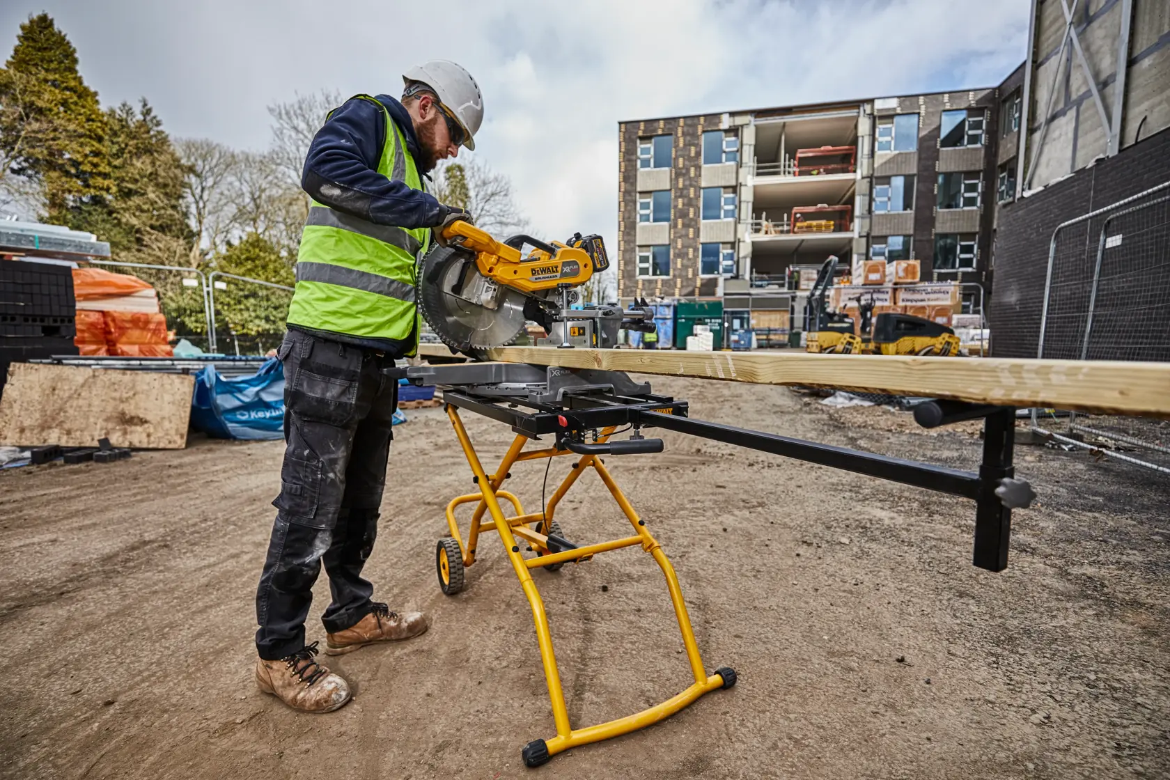 Arbeiter nutzt DEWALT DE7260 Sägeständer zum Holzzuschnitt auf Baustelle. Gebäude im Hintergrund.