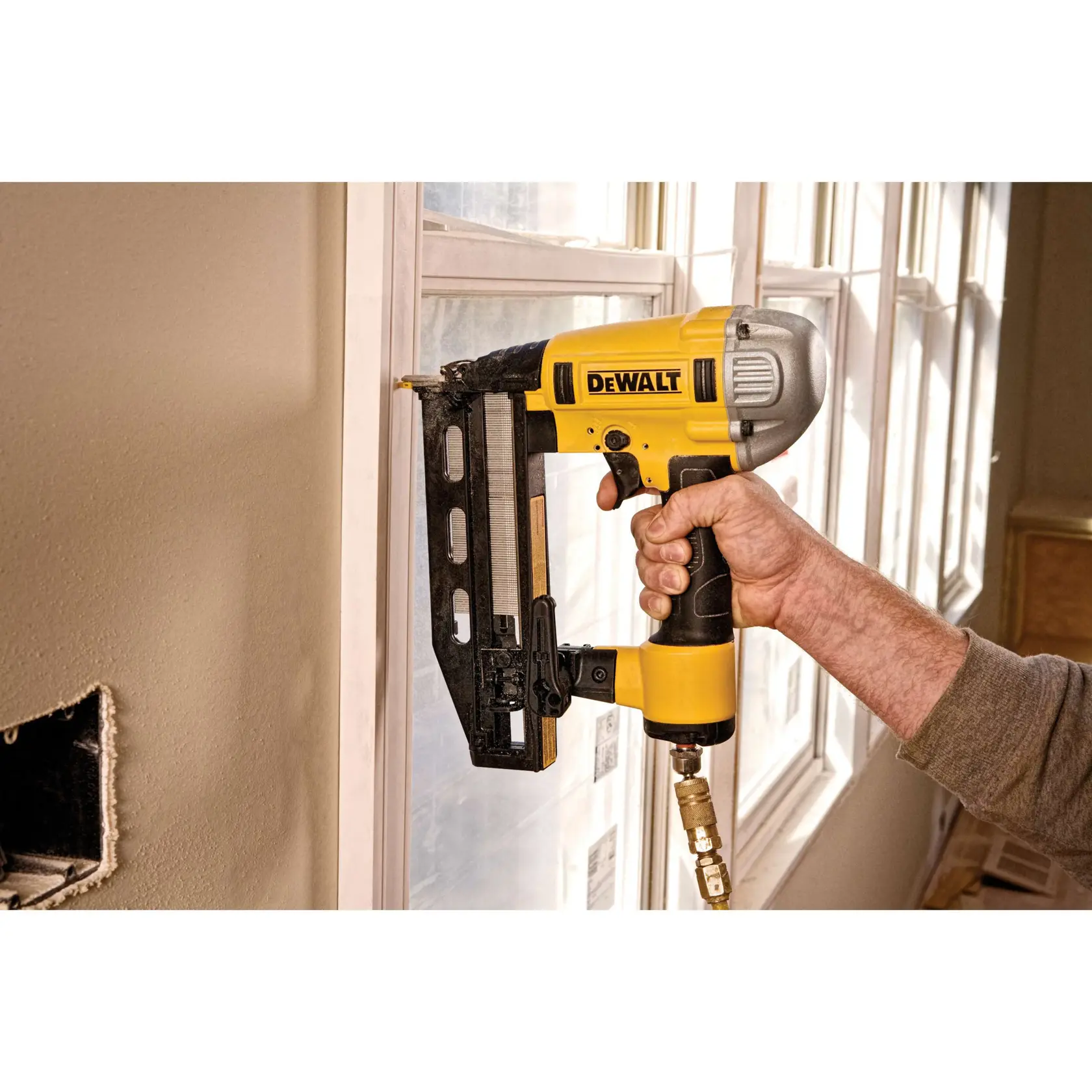 DEWALT pneumatischer Nagler befestigt Zierleisten an einem Fensterrahmen bei Bauarbeiten.