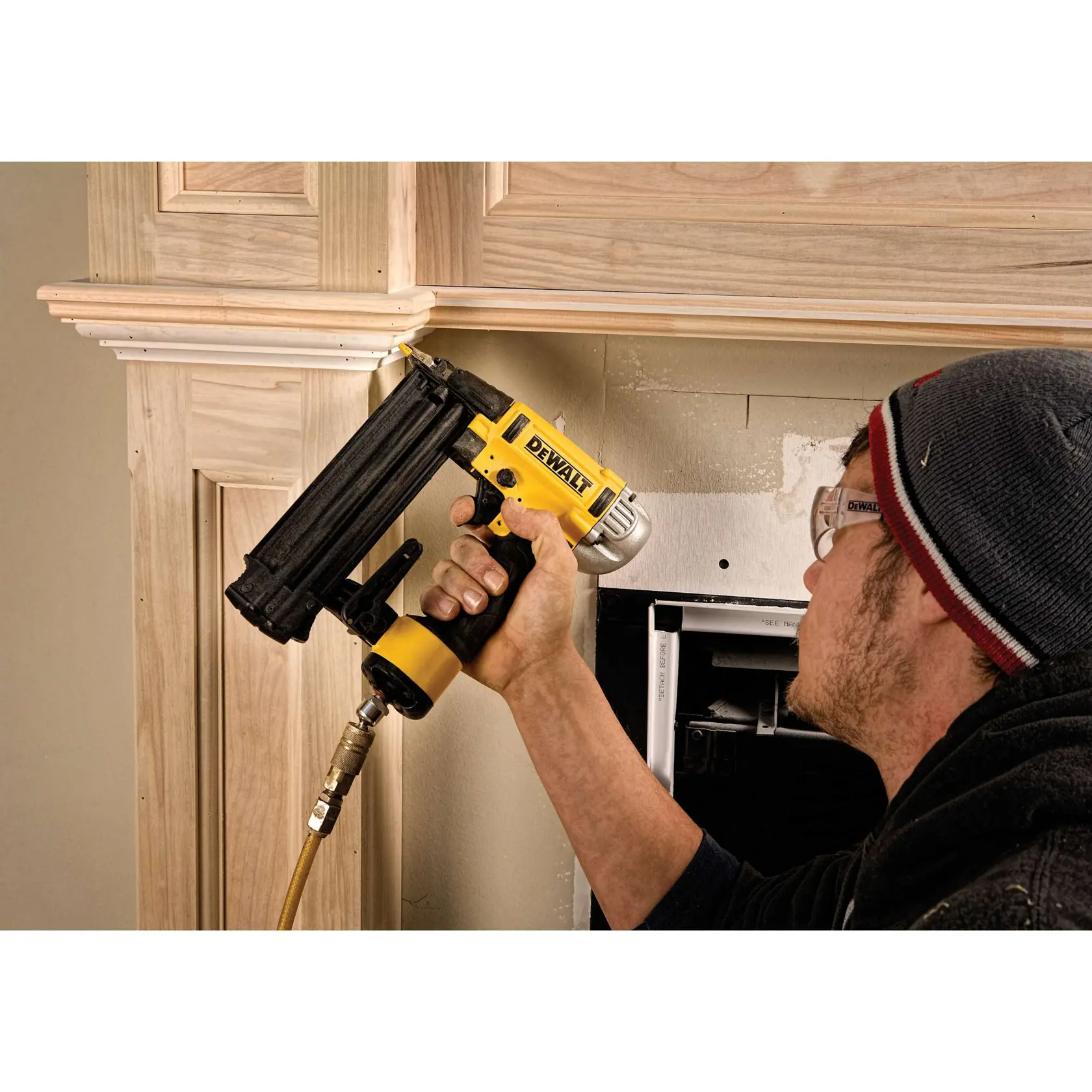 Person befestigt Holzleiste mit DEWALT Nagler, trägt Schutzbrille und Mütze.