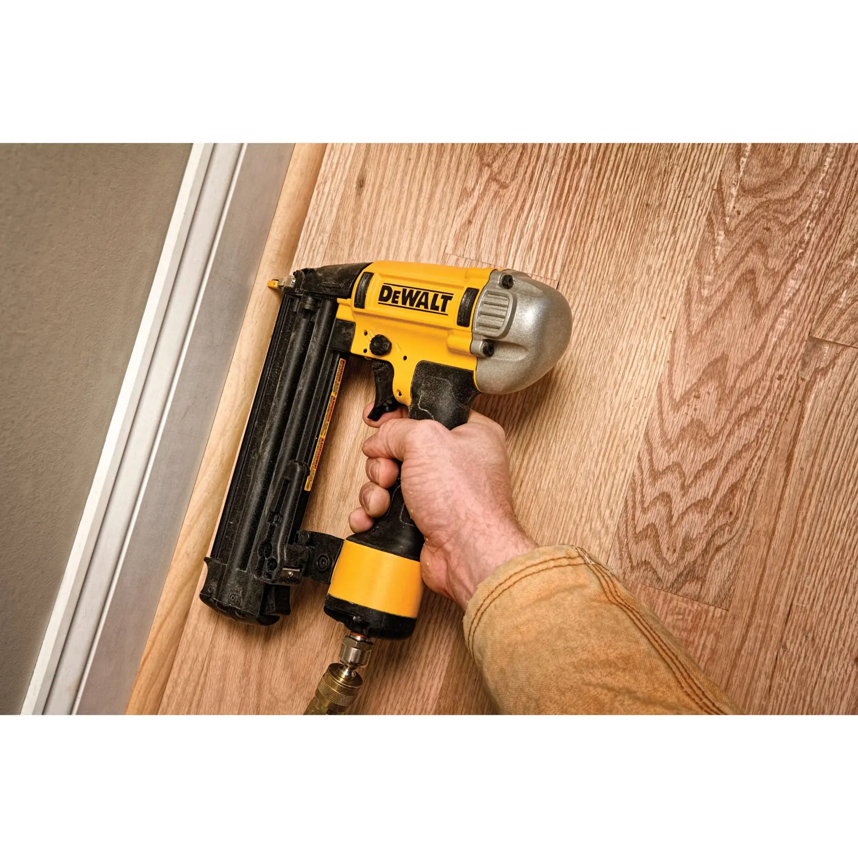 Hand verwendet einen DEWALT Nagler auf einem Holzboden neben einer Wand.