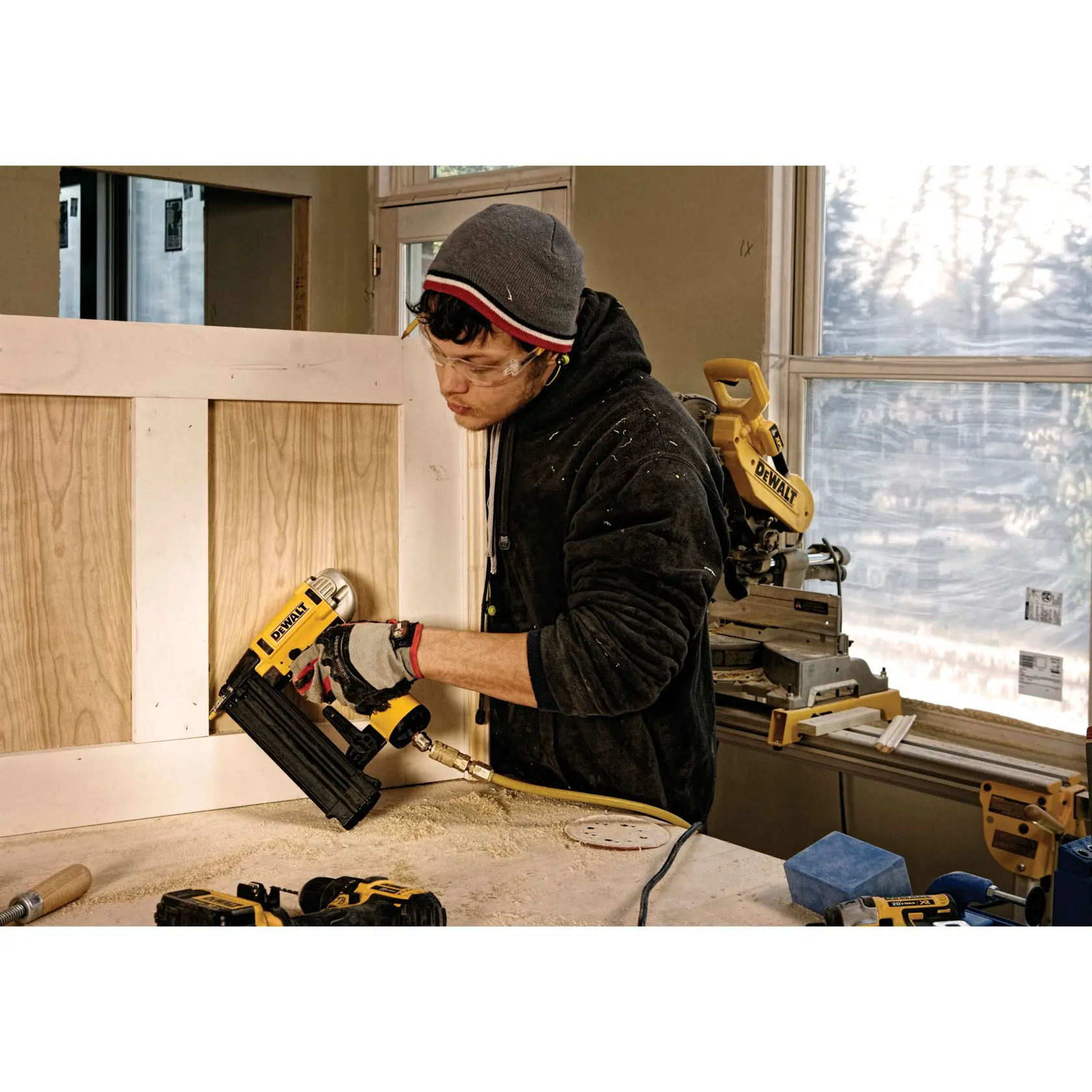 Person nutzt DEWALT Nagler zum Befestigen eines Panels in der Werkstatt. Weitere DEWALT Werkzeuge sichtbar.