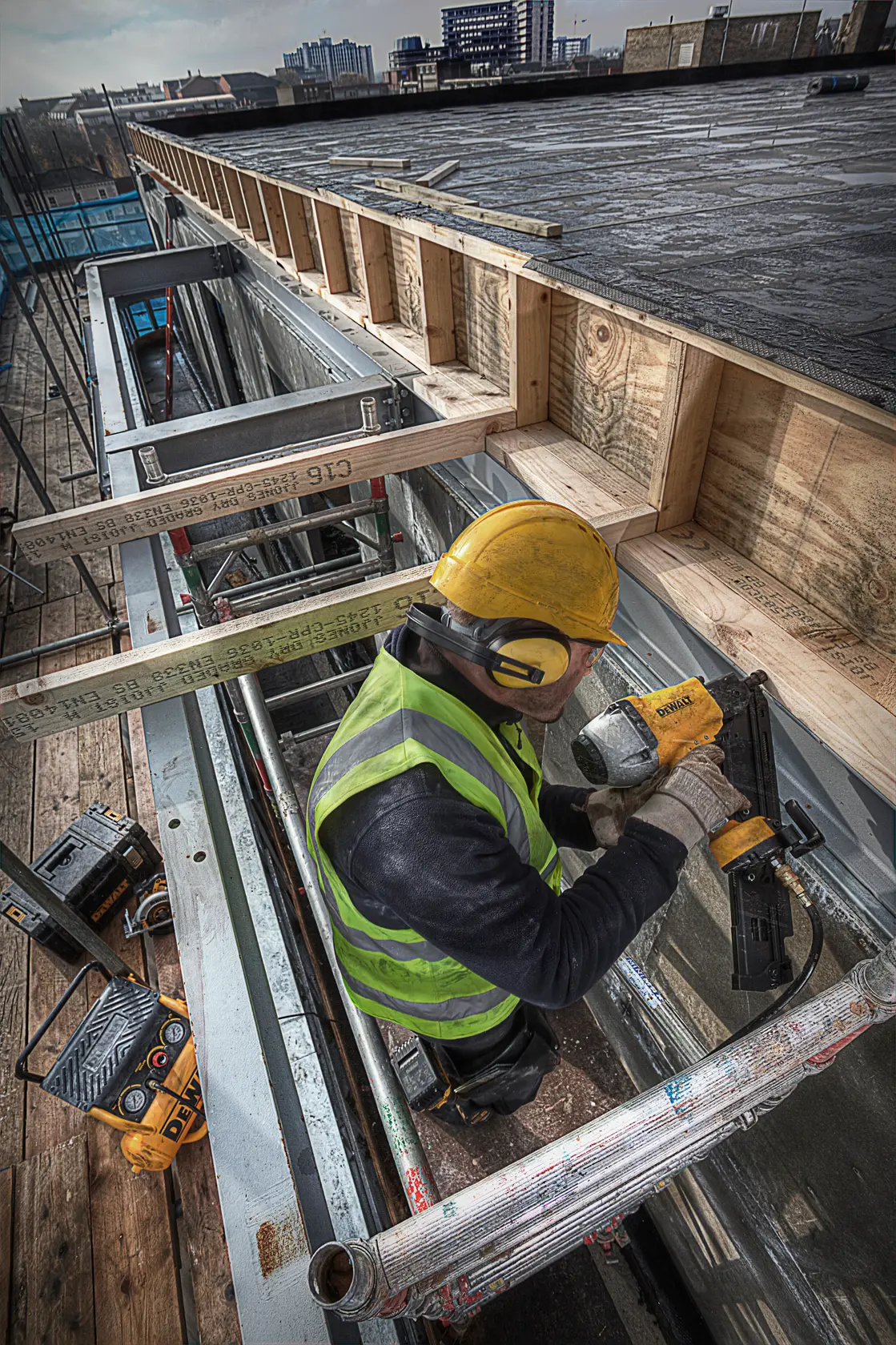 Arbeiter mit Schutzkleidung nutzt DEWALT Nagelpistole auf Baustelle mit Holz- und Metallrahmen.