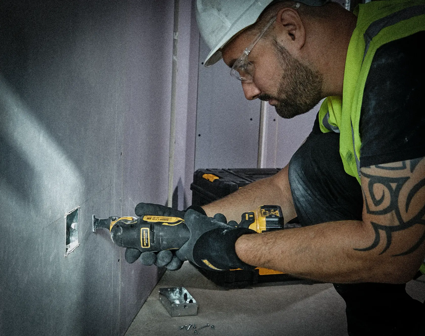Person schneidet Trockenbau mit DEWALT Multi-Tool. Werkzeugkoffer und Schrauben sind am Boden sichtbar.