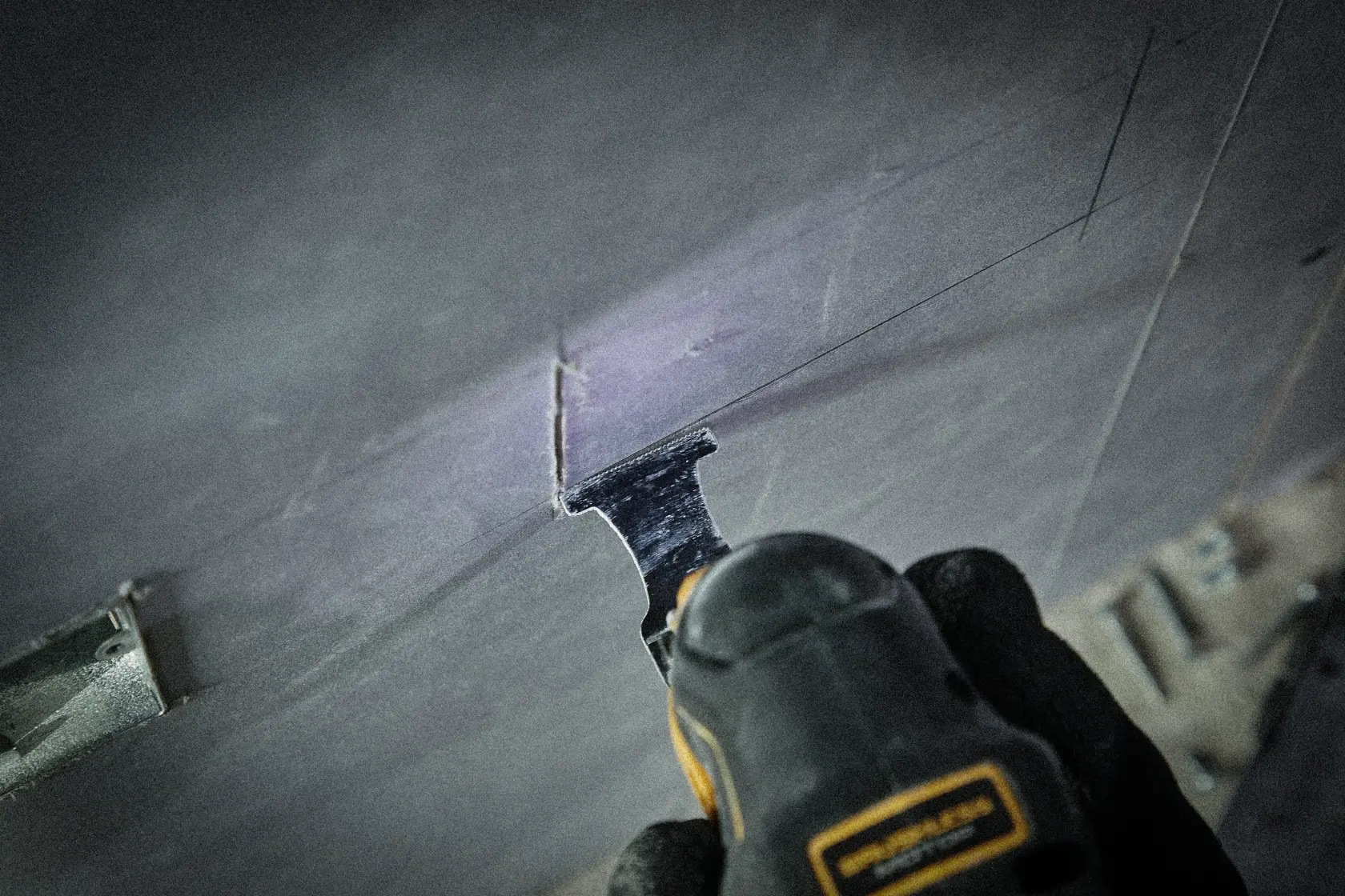 DEWALT oszillierendes Werkzeug schneidet ein Rechteck in Wand oder Platte, Bediener mit Handschuhen.