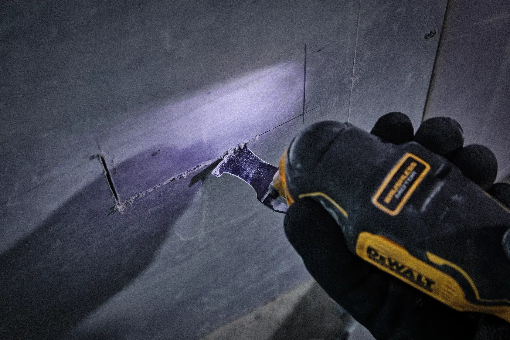 DEWALT Werkzeug schneidet rechteckiges Loch in Trockenbauwand, gehalten von Handschuh, mit LED-Licht.