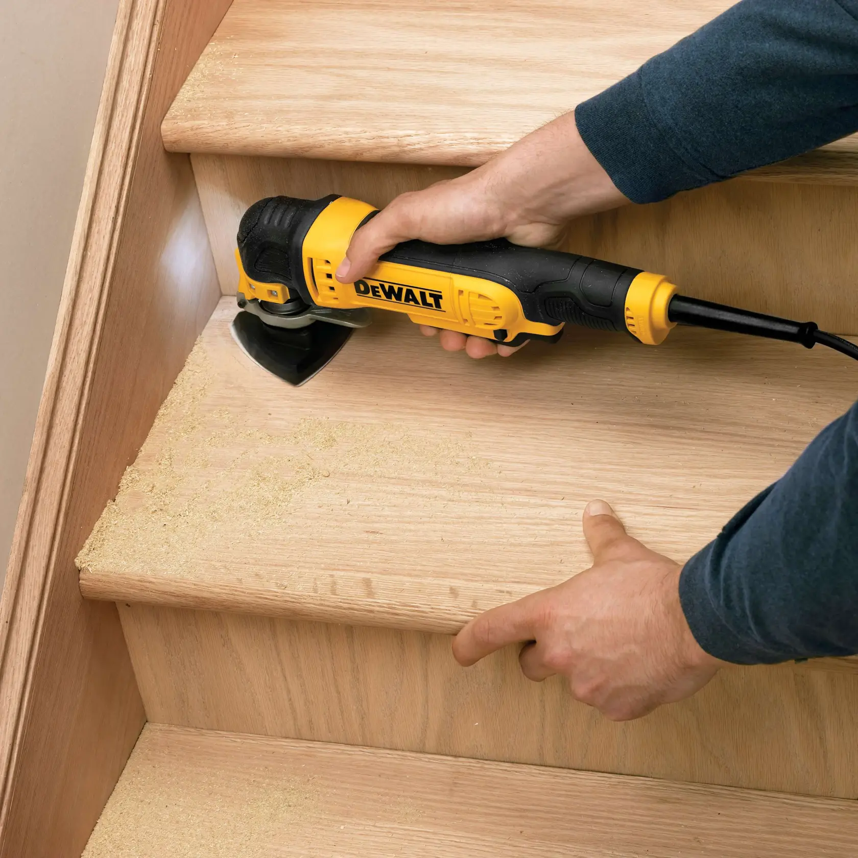 Persona lijando escalera de madera con herramienta DEWALT, hay aserrín en los peldaños.