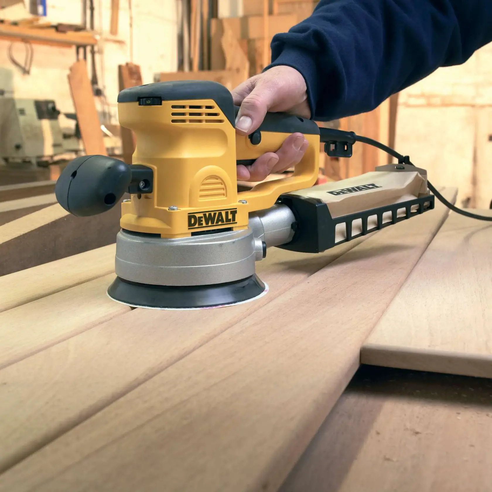 DEWALT Schleifmaschine im Einsatz auf Holzplatten in einer Werkstatt, von einer Hand gehalten.
