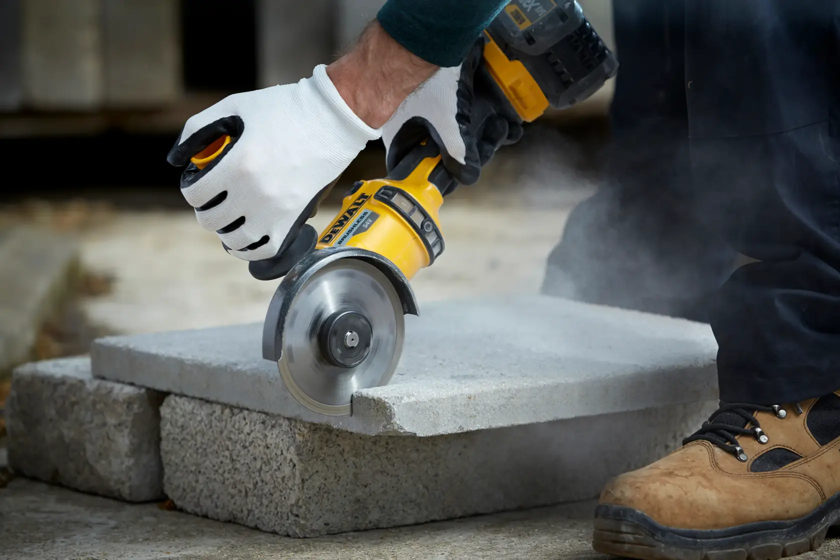 Eine behandschuhte Hand schneidet eine Betonplatte mit einem DEWALT Werkzeug, Staub entsteht.