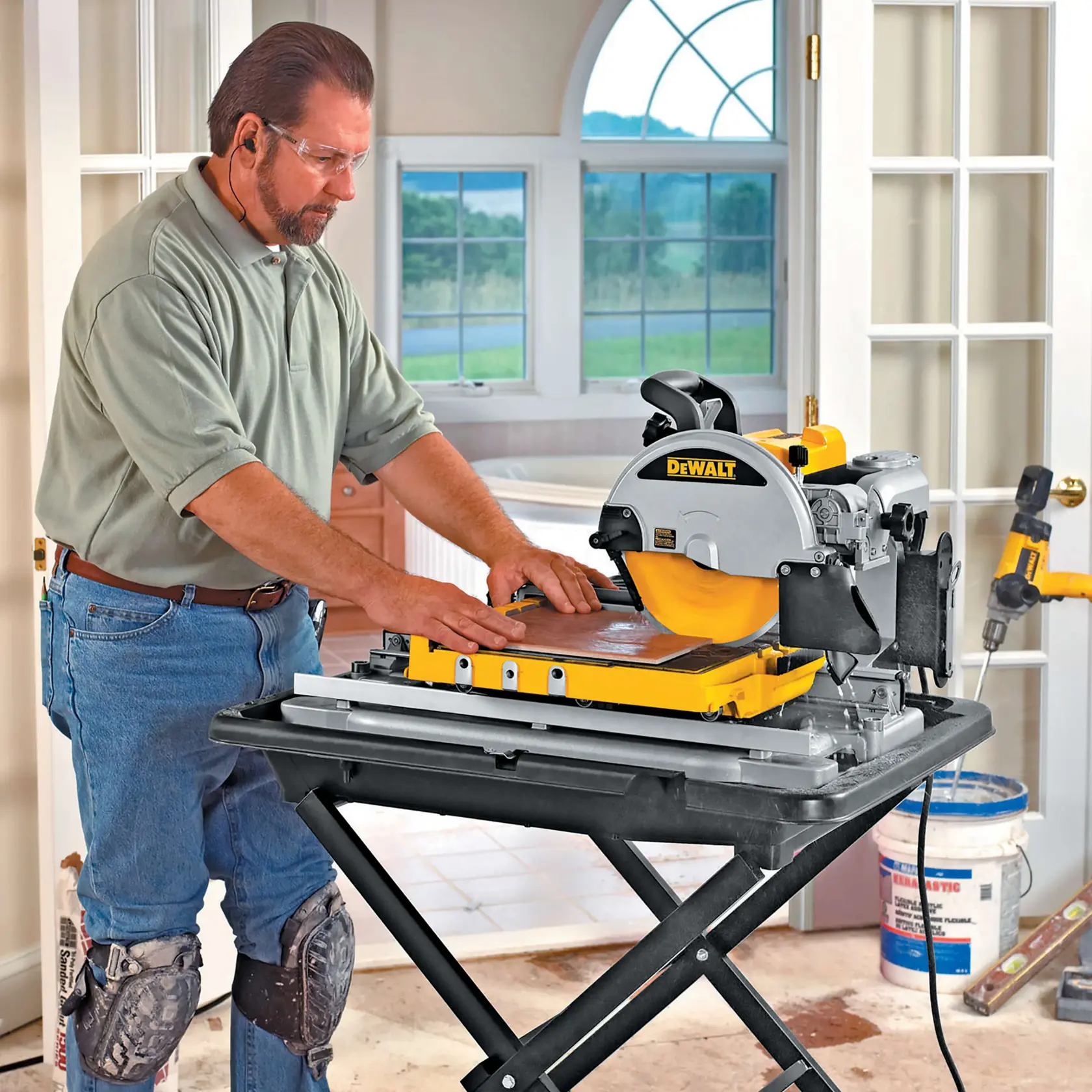 Persona corta azulejos en interior con sierra DEWALT DT3733, usando rodilleras y protección auditiva.