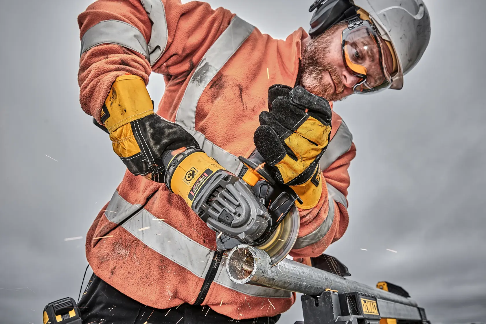 Trabajador corta un tubo metálico con amoladora DEWALT, protegido con guantes y casco.