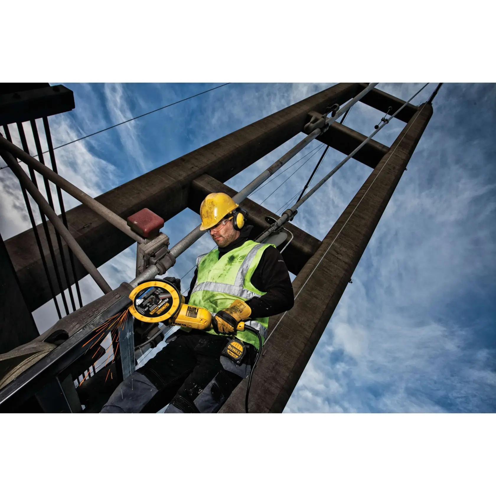 Trabajador corta metal en un puente con herramienta DEWALT, usando casco y equipo de seguridad.