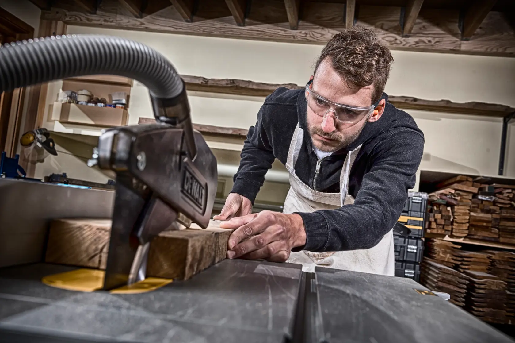 Persona cortando madera con sierra DEWALT en taller, lleva delantal y está concentrada.