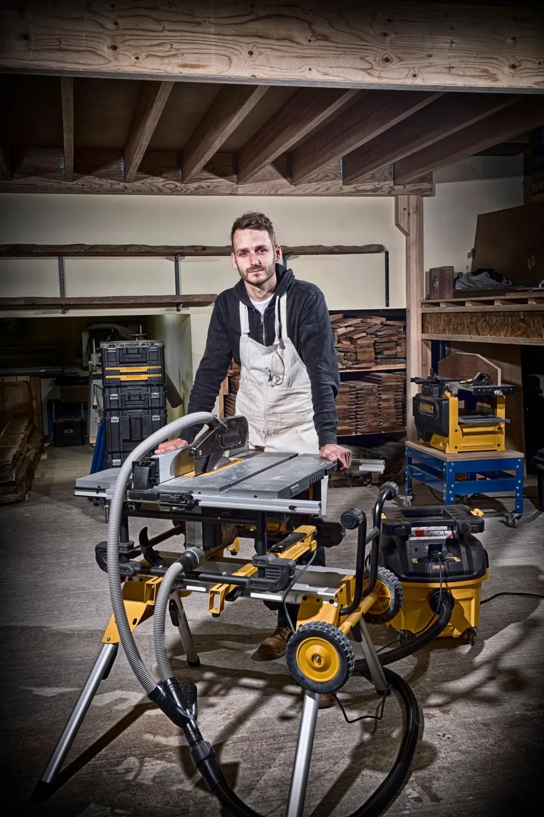 Persona en taller con sierra DEWALT DT4351 en soporte y sistema de extracción, rodeada de madera y herramientas.