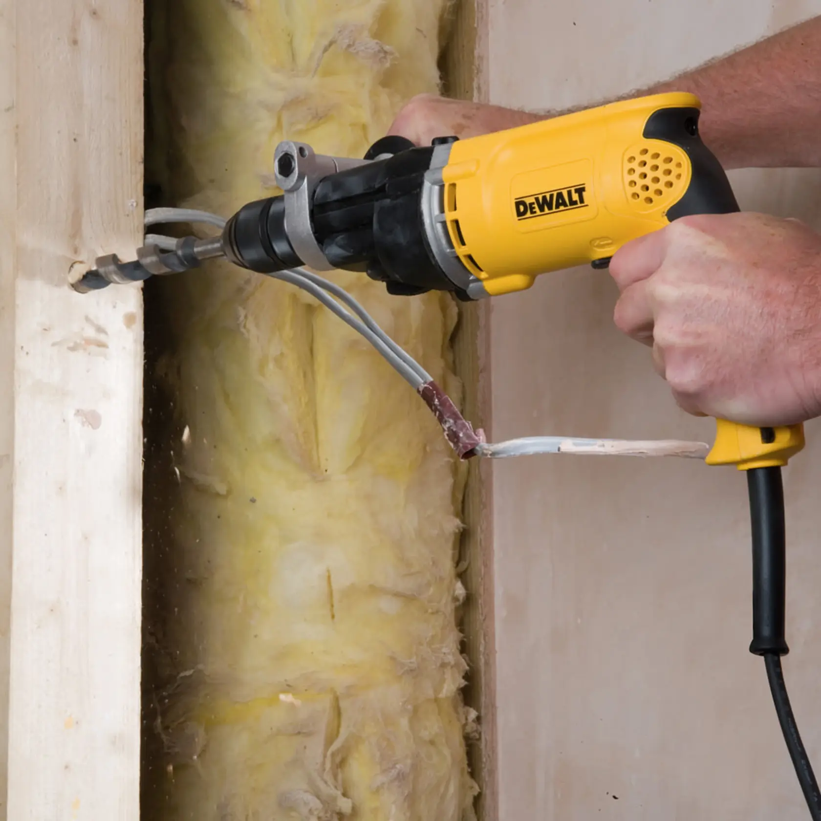 Eine DEWALT-Bohrmaschine bohrt ein Loch in Holz, umgeben von Isolierung und elektrischen Leitungen.
