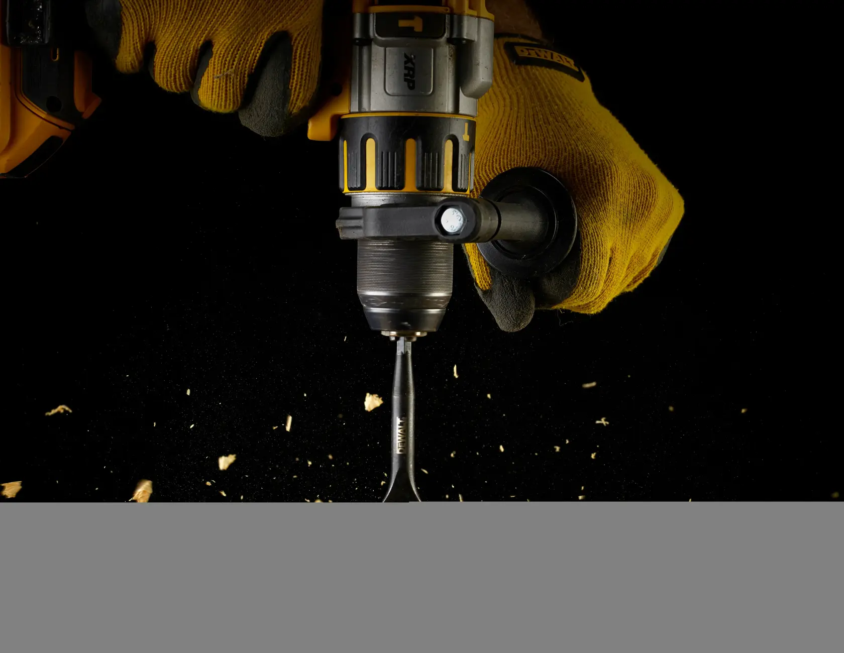 Manos con guantes usan taladro DEWALT y broca tipo pala para perforar madera con virutas.
