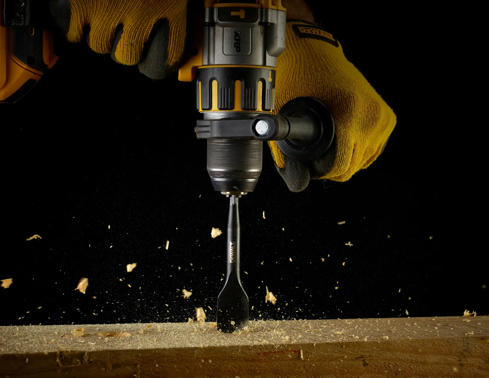 Taladro DEWALT con broca plana perfora viga de madera, saltan chispas, manos con guantes negros.