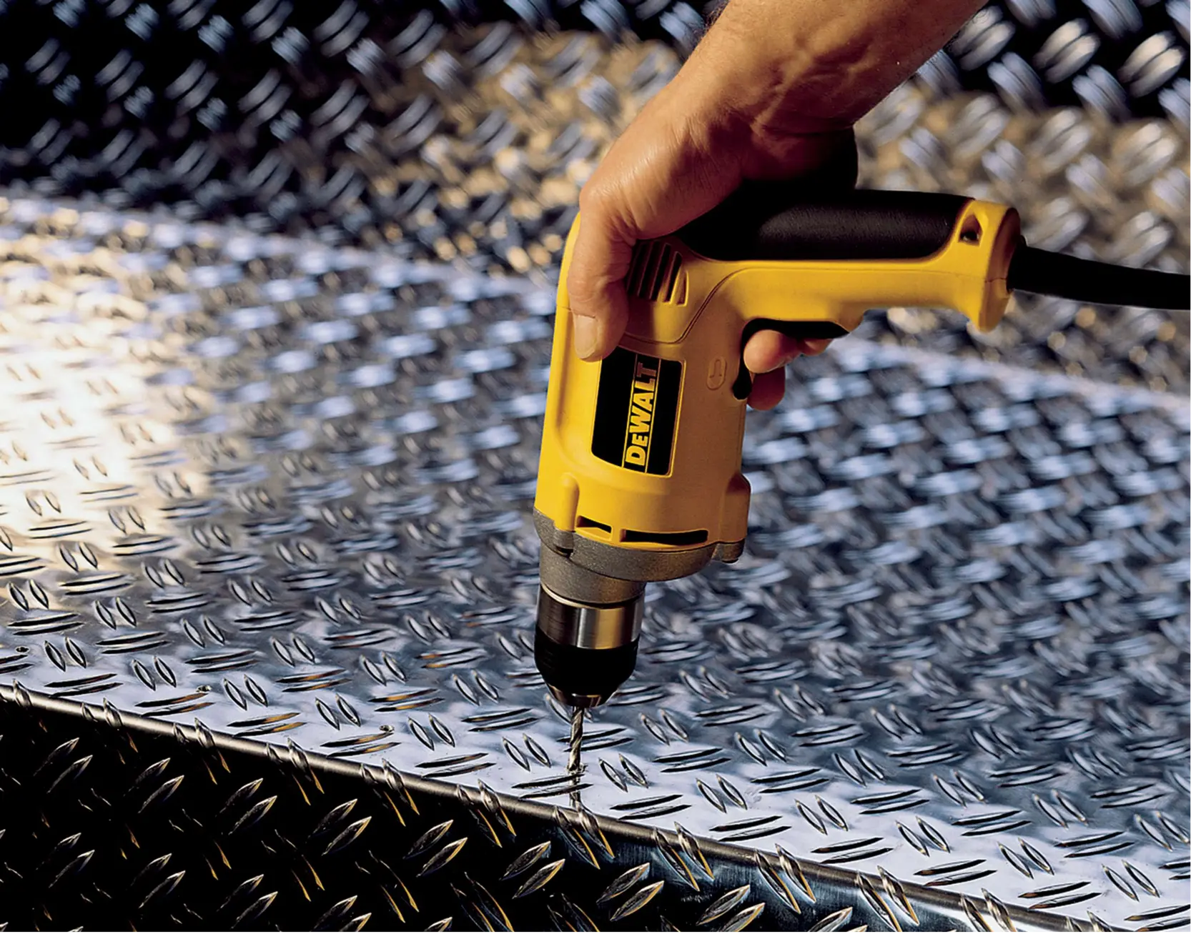 Un taladro DEWALT perfora una placa metálica con superficie texturizada.