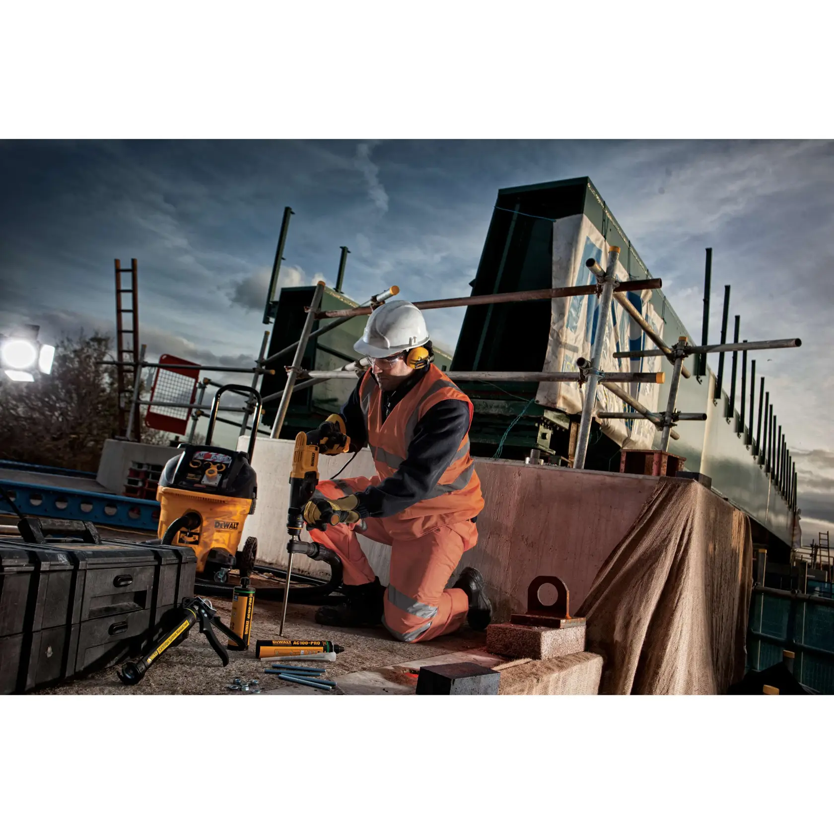 Trabajador usa taladro DEWALT en obra, con equipo de seguridad y rodeado de herramientas DEWALT.