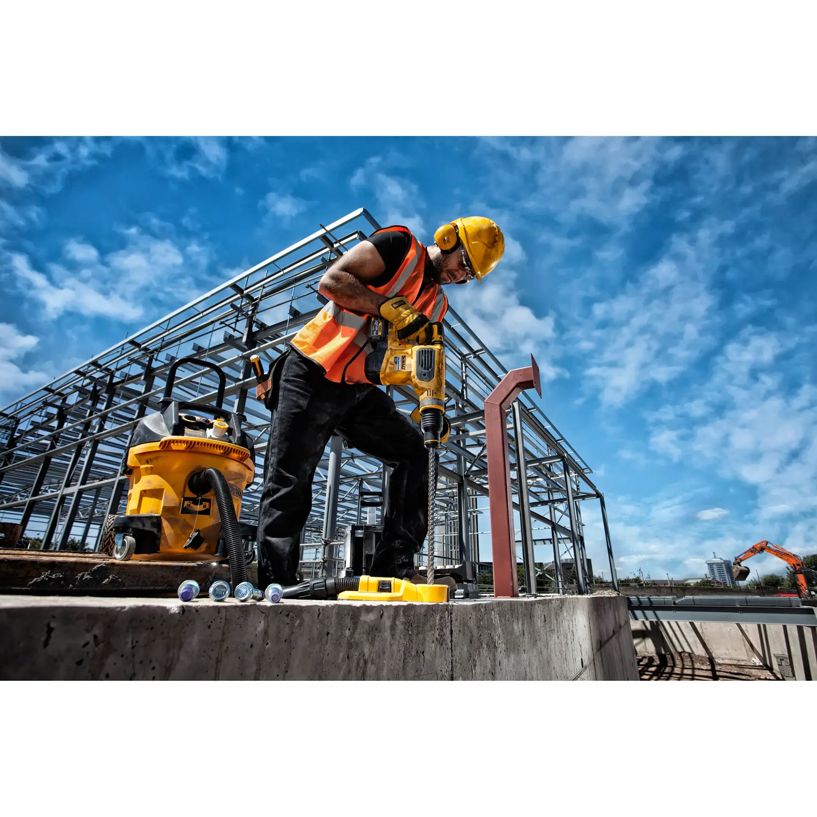 Trabajador usa taladro DEWALT amarillo en obra de acero al aire libre, con casco y chaleco de seguridad.