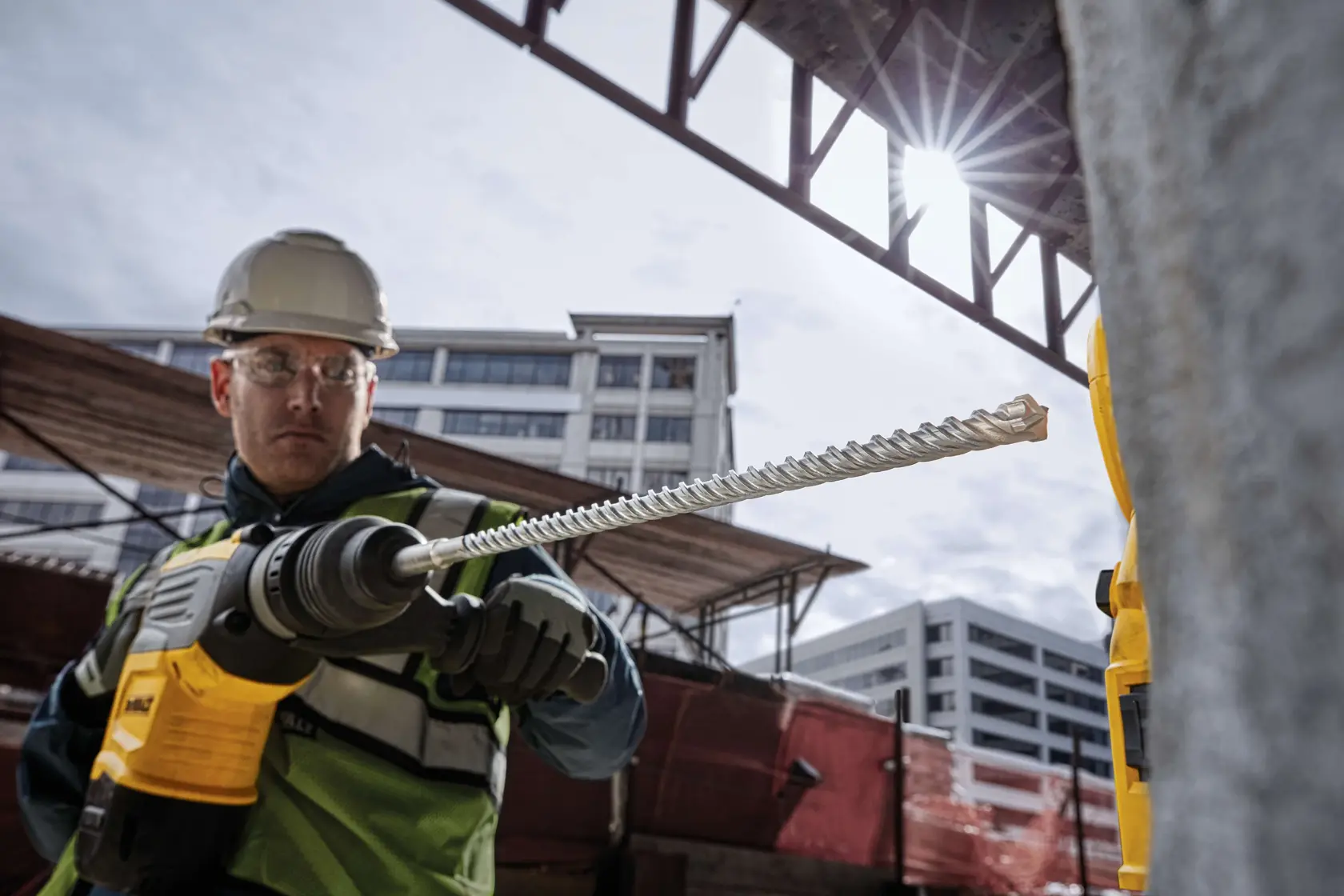 Persona usa taladro DEWALT amarillo con extractor para perforar concreto en obra.
