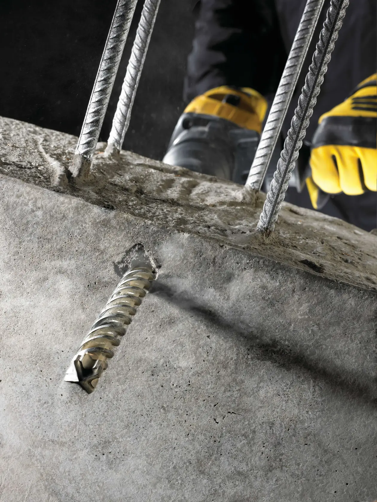DEWALT-Bohrer durchdringt Beton mit Stahlstäben, bedient von einem Arbeiter mit gelben Handschuhen.