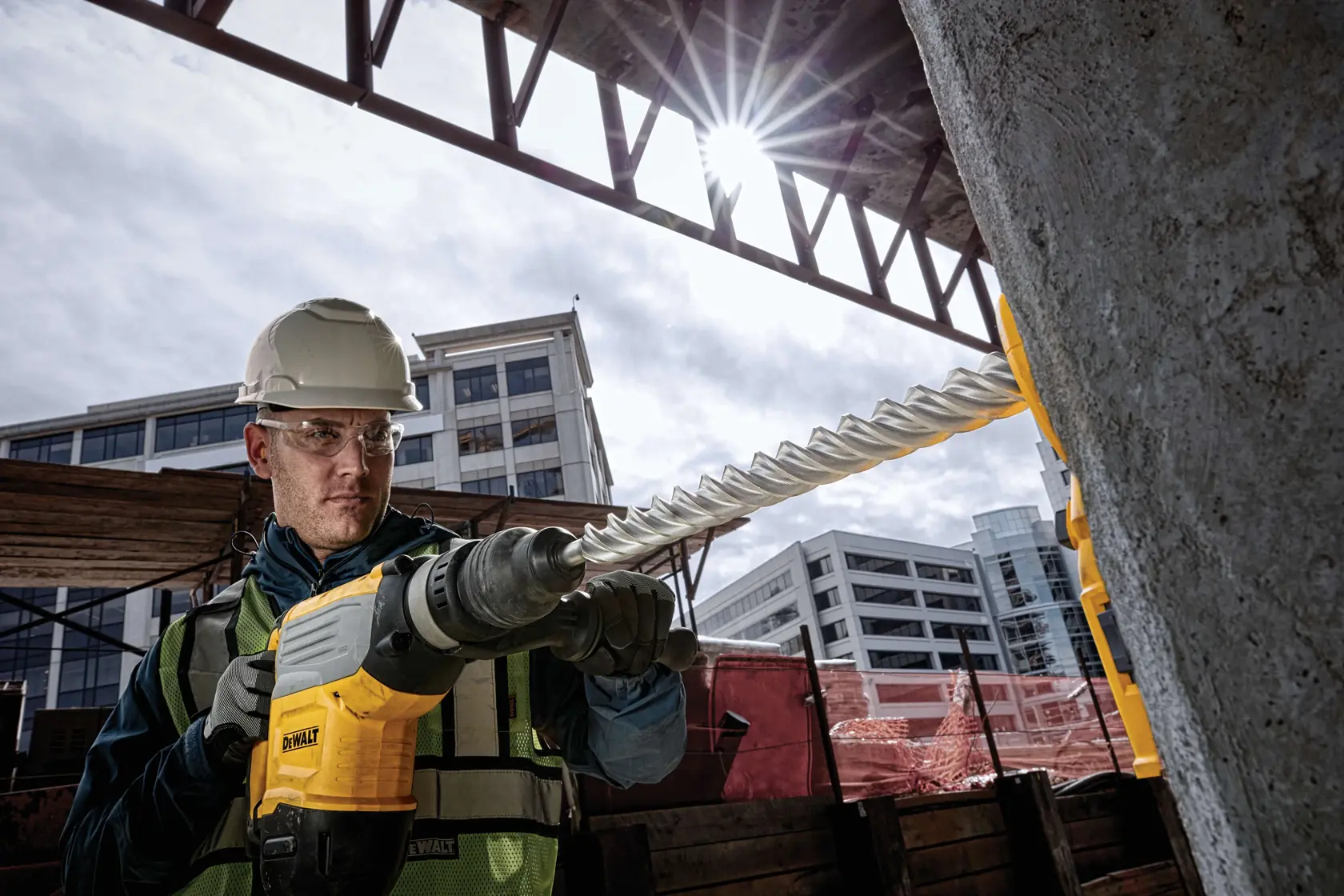 Taladro DEWALT en uso en obra, perforando concreto. Trabajador con equipo de seguridad. Edificios urbanos detrás.