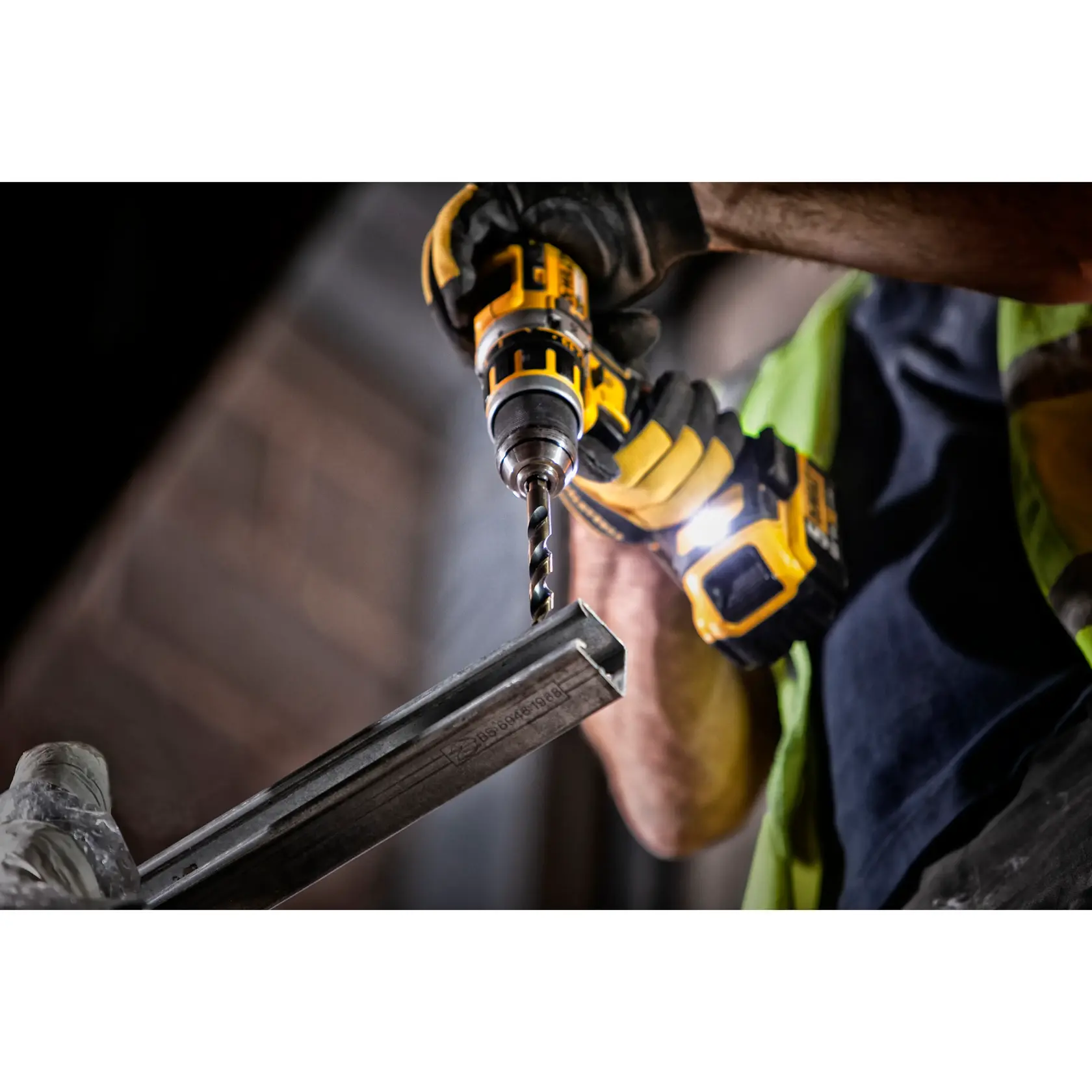 Nahaufnahme einer DEWALT-Bohrmaschine, die von einem Arbeiter mit Handschuhen in Metall bohrt.