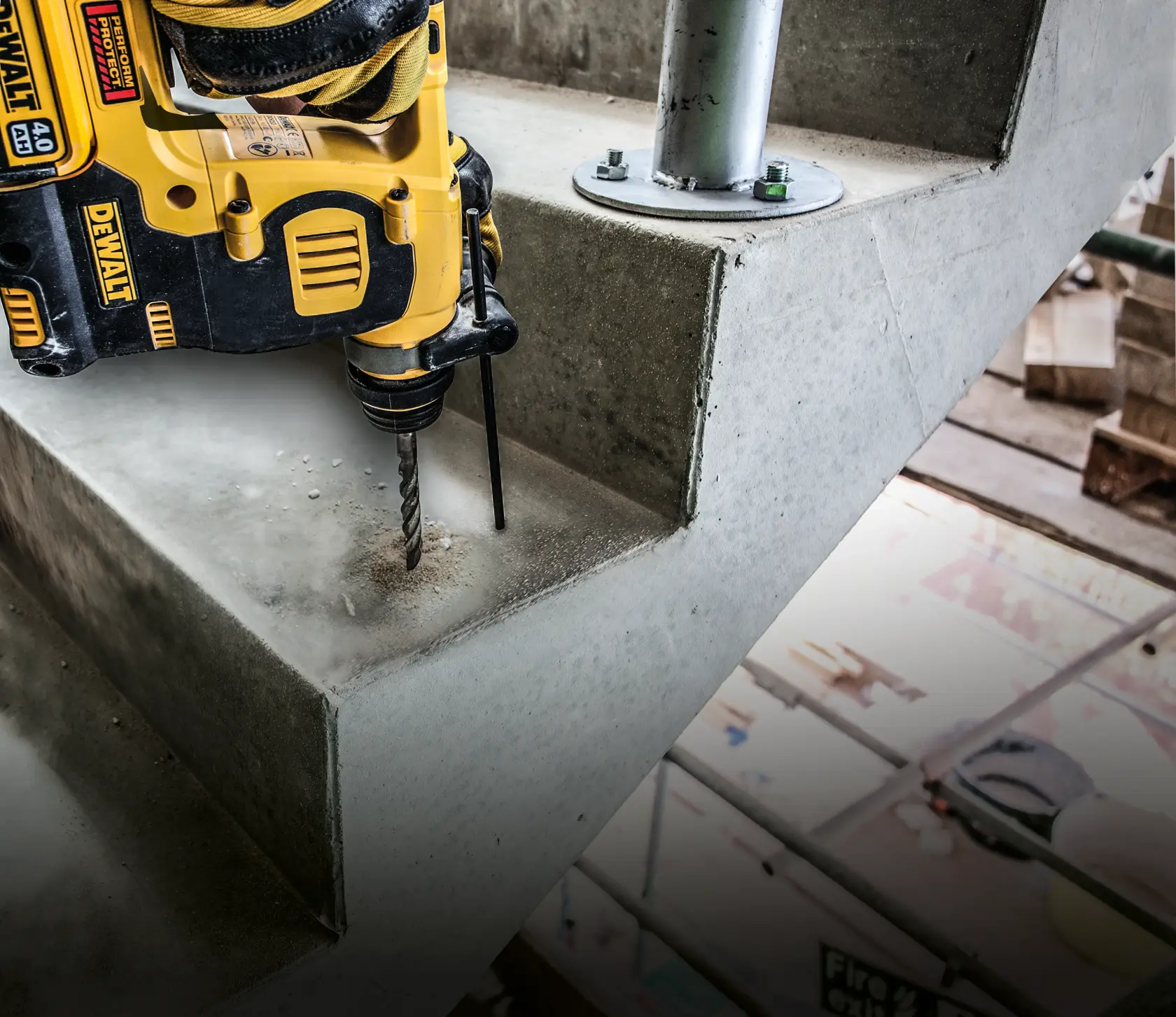 Taladro DEWALT perforando escalera de concreto, haciendo agujero junto a poste metálico en obra interior.