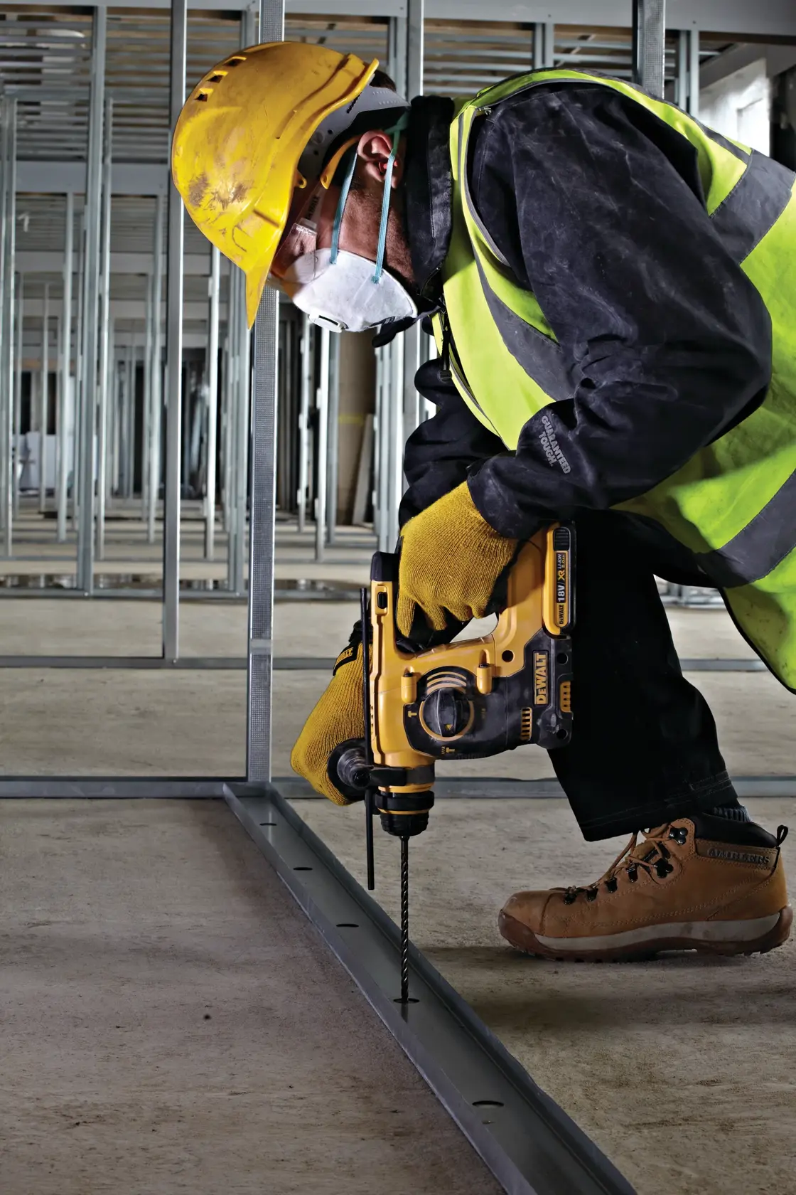Trabajador usa taladro DEWALT en marco metálico, con equipo de seguridad y mascarilla en obra.