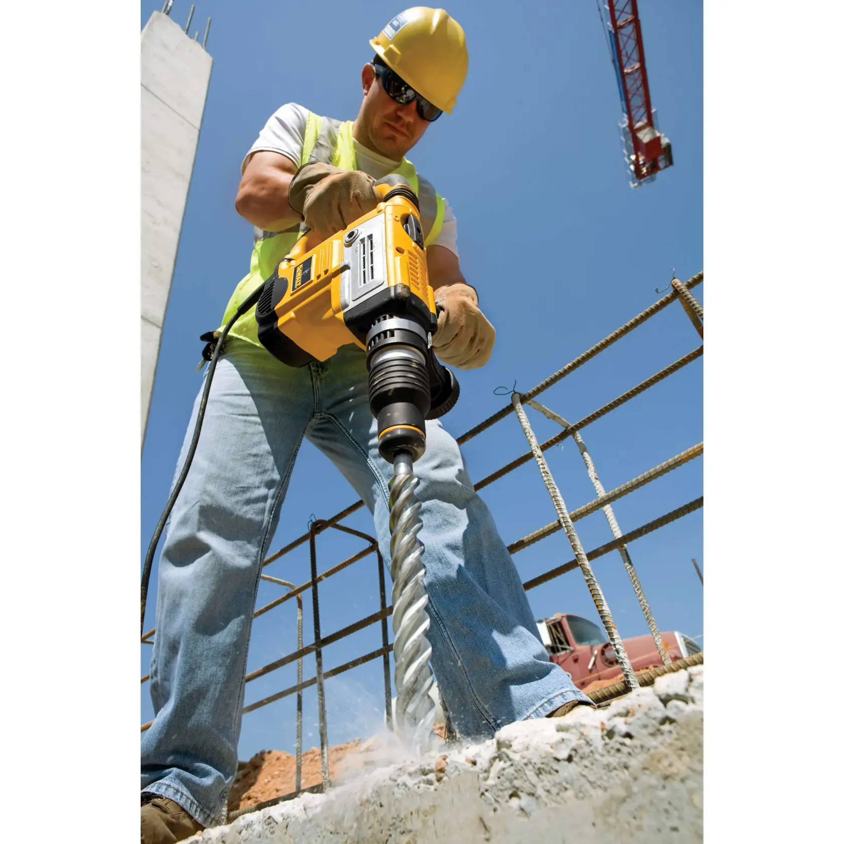 Arbeiter nutzt DEWALT-Bohrer DT9426, DT9426-QZ auf Baustelle. Beton und Bewehrung sichtbar.