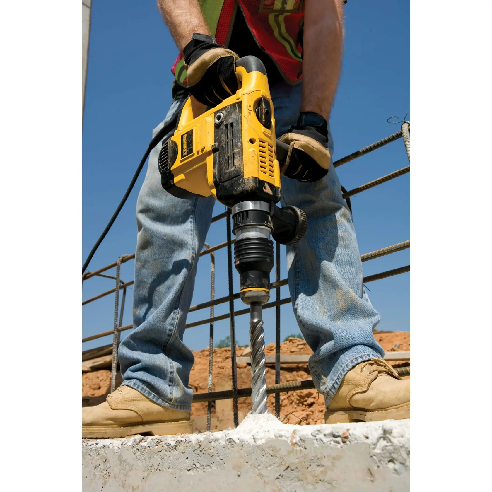 Person bohrt mit einem DEWALT Hammer auf Beton an einer Baustelle, trägt Handschuhe und Stiefel.