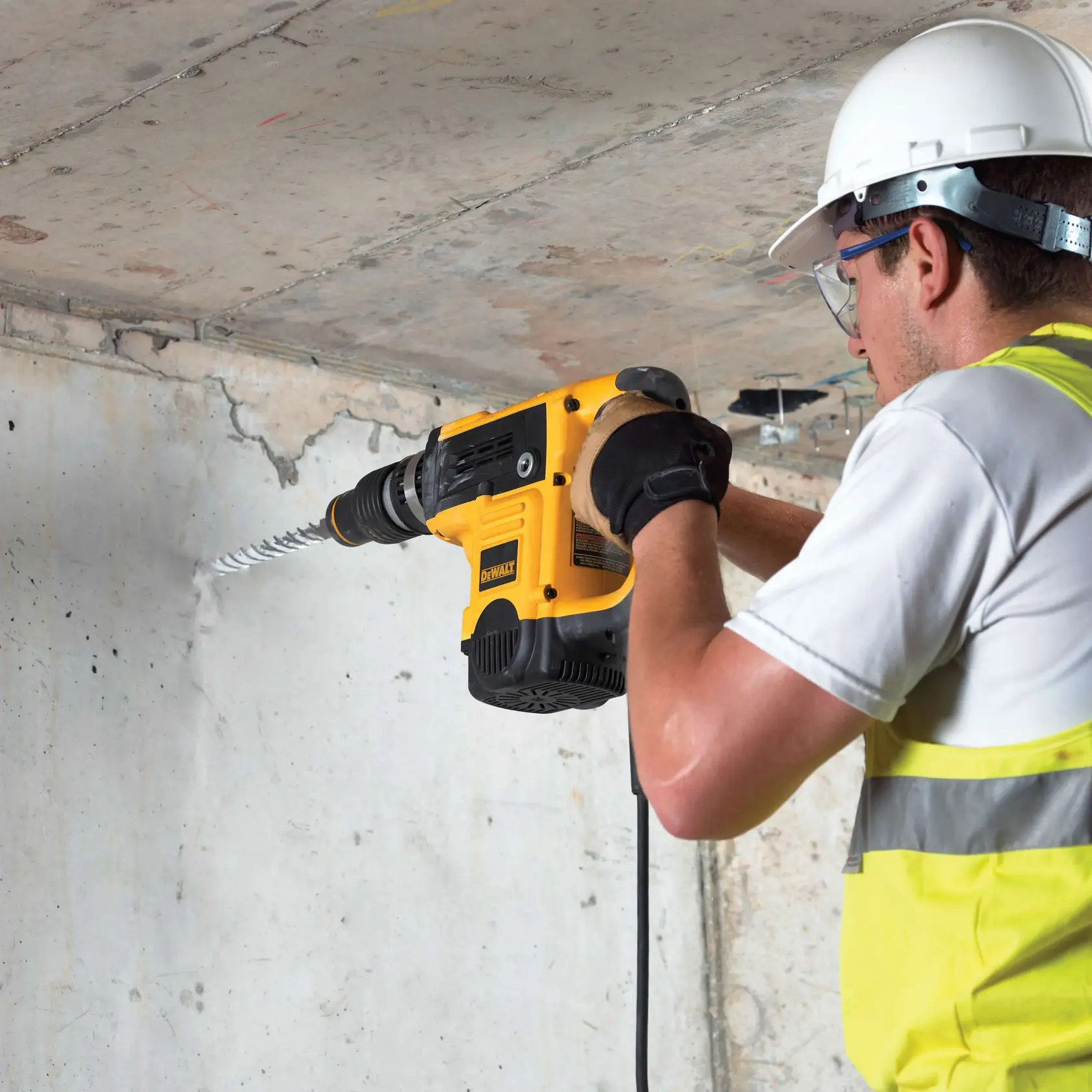 Arbeiter bohrt Betonwand mit gelber DEWALT-Bohrmaschine, trägt Helm und Handschuhe.