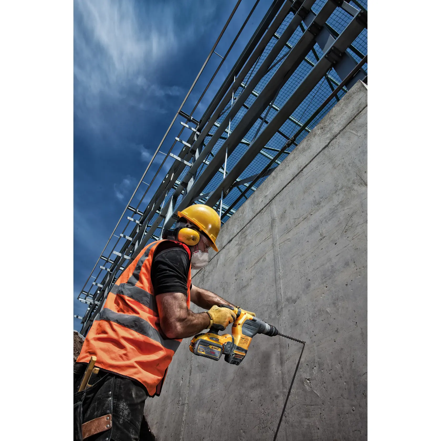Trabajador con equipo de seguridad utiliza taladro DEWALT en muro de concreto en obra bajo cielo azul.