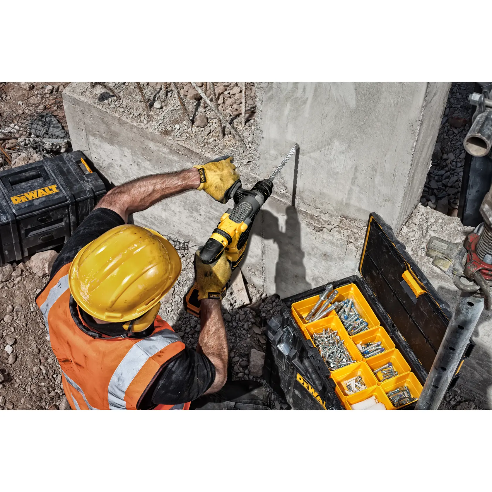 Trabajador perfora muro de concreto con taladro DEWALT, cajas de herramientas y tornillos en obra.