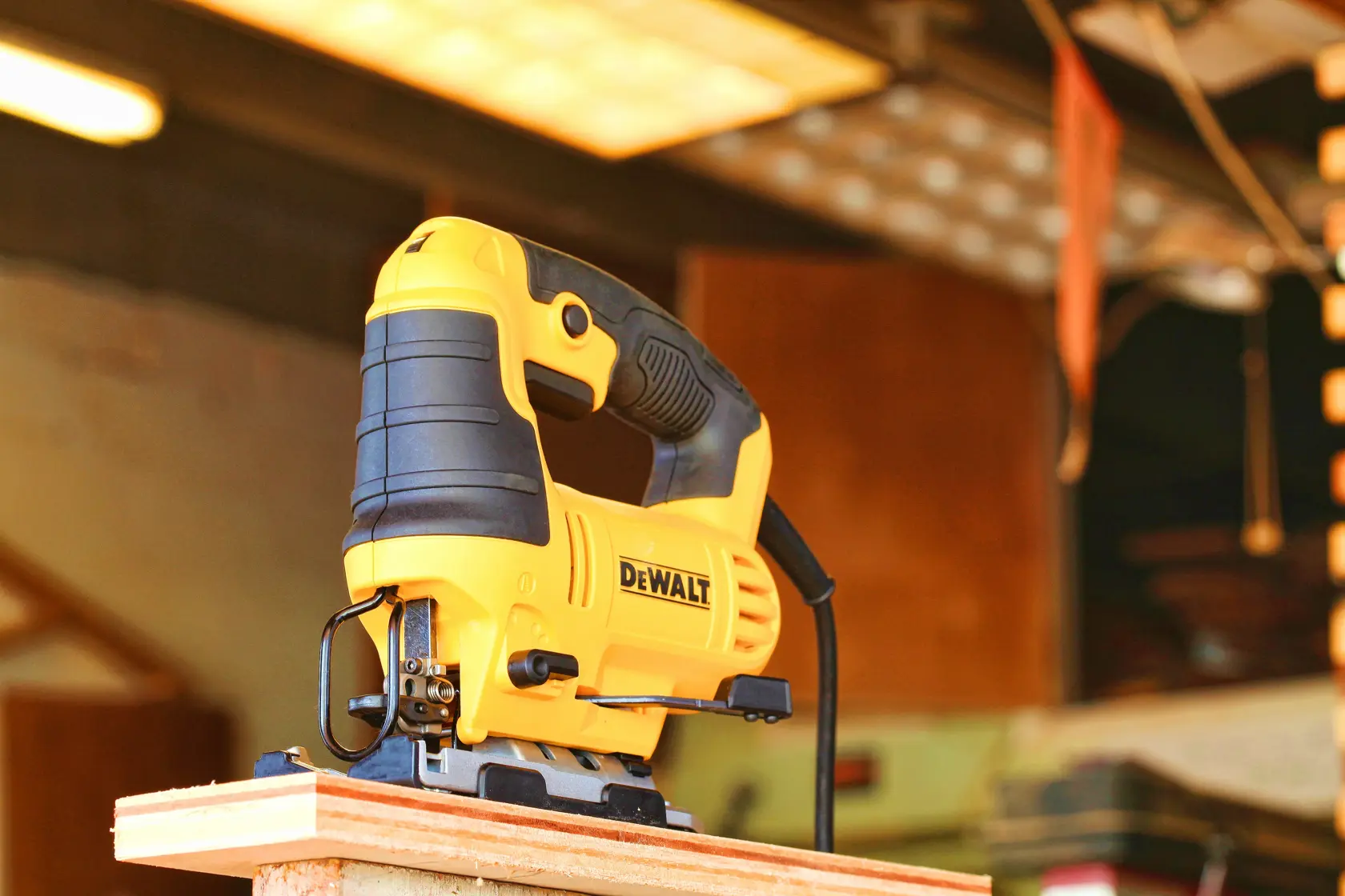 Eine gelb-schwarze elektrische Stichsäge von DEWALT steht am Rand eines Holzstücks in einer Werkstatt.