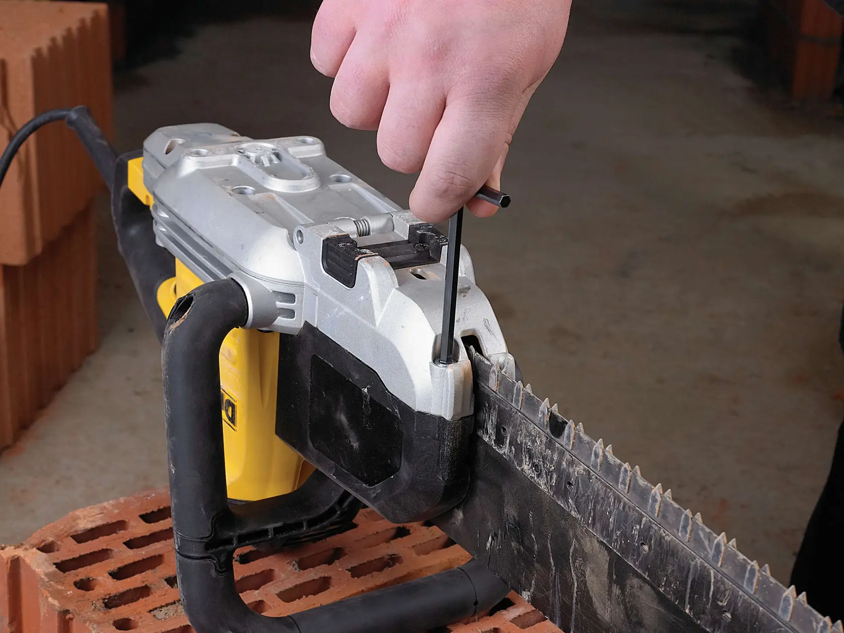 Hand stellt das Sägeblatt einer DEWALT Elektrosäge auf einem Ziegel mit Werkzeug ein.