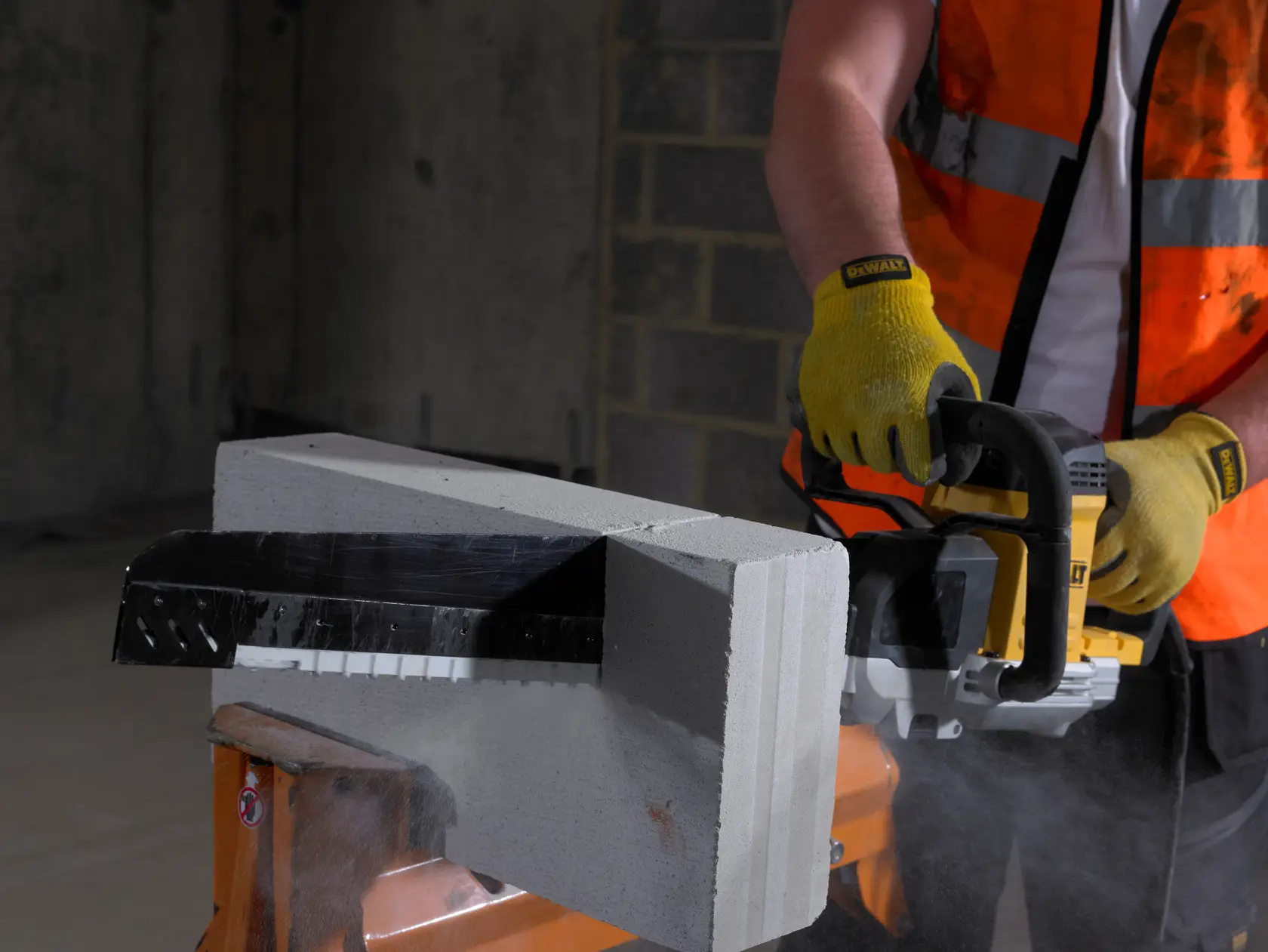 Arbeiter schneidet Betonblock mit DEWALT Säge, trägt Handschuhe und Sicherheitsweste, Staub sichtbar.
