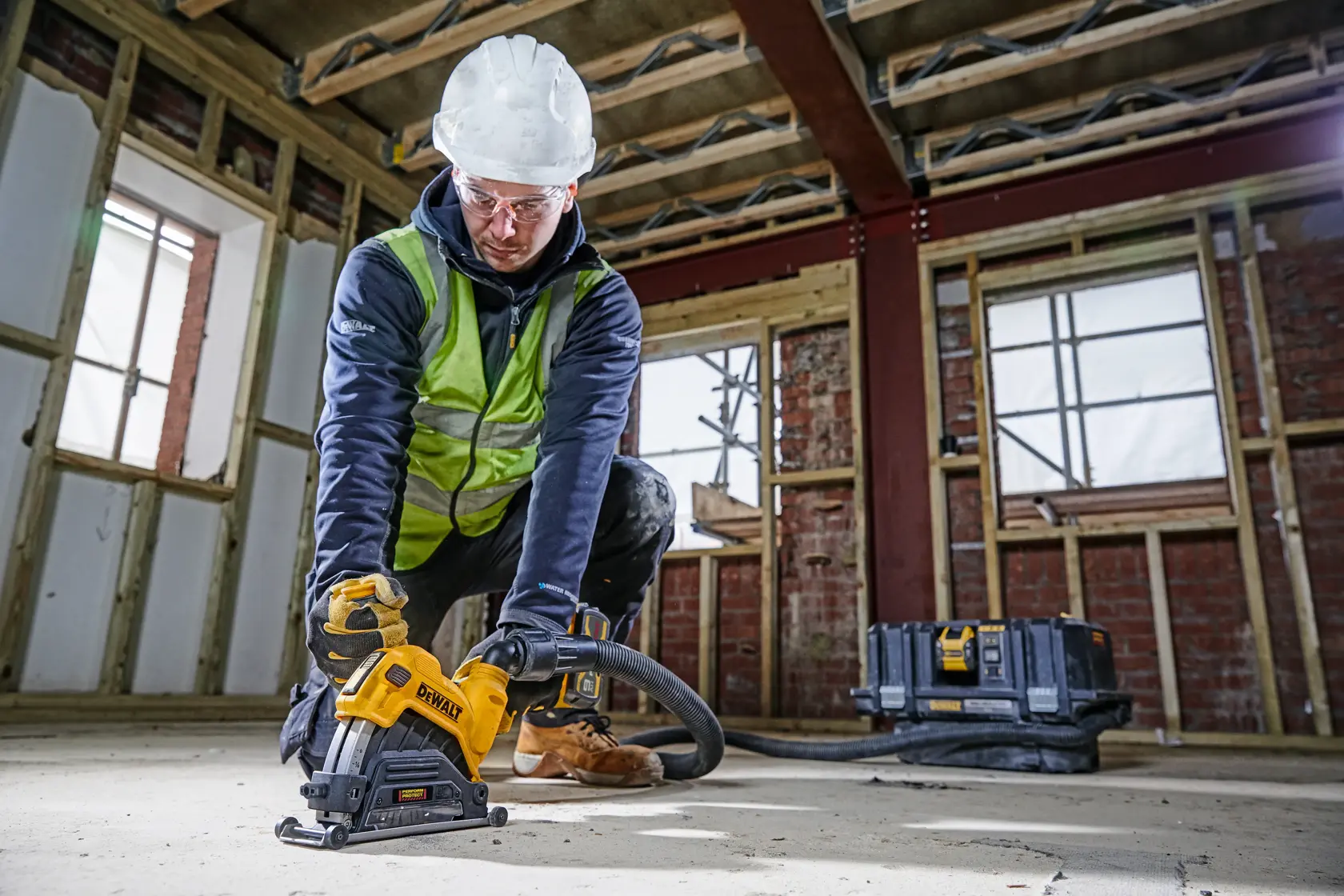 Arbeiter nutzt DEWALT DWE46225 Säge auf Baustelle, trägt Schutzkleidung und schneidet Betonboden.
