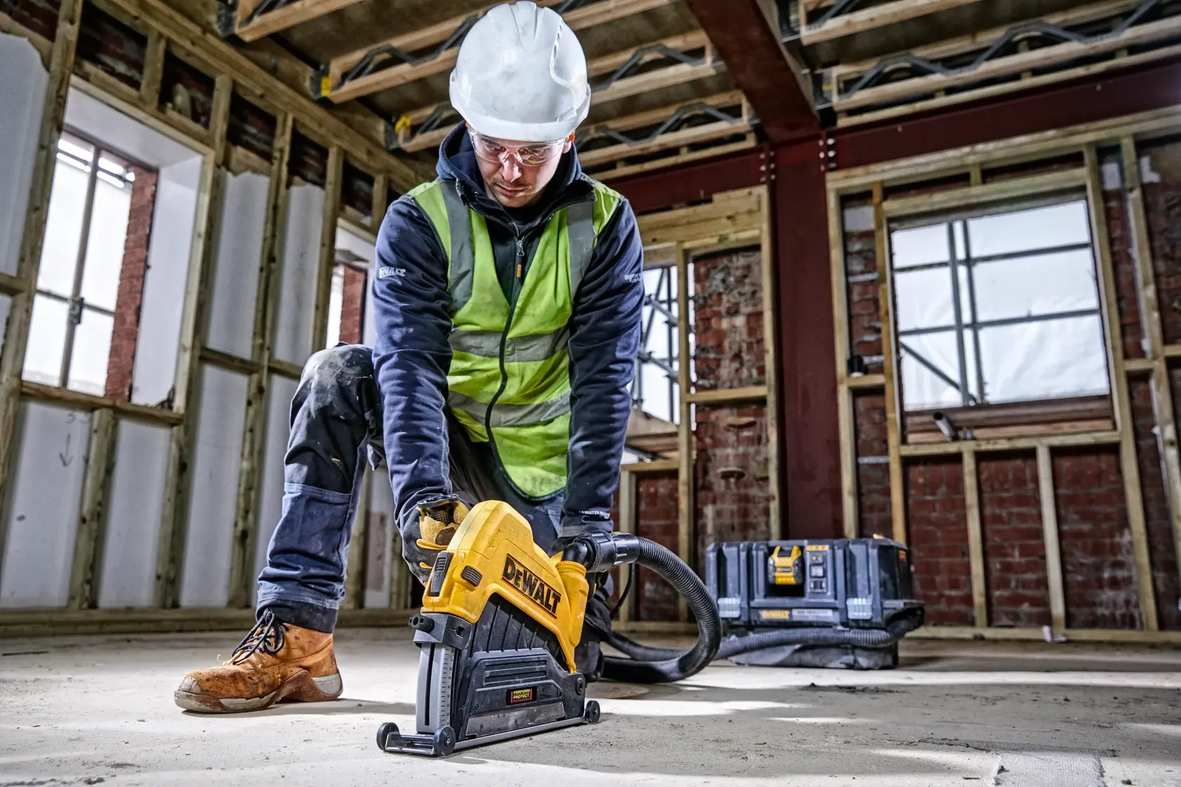 Arbeiter nutzt DEWALT Schneidwerkzeug am Boden auf Baustelle, mit Schutzkleidung. Werkzeugkasten hinten.