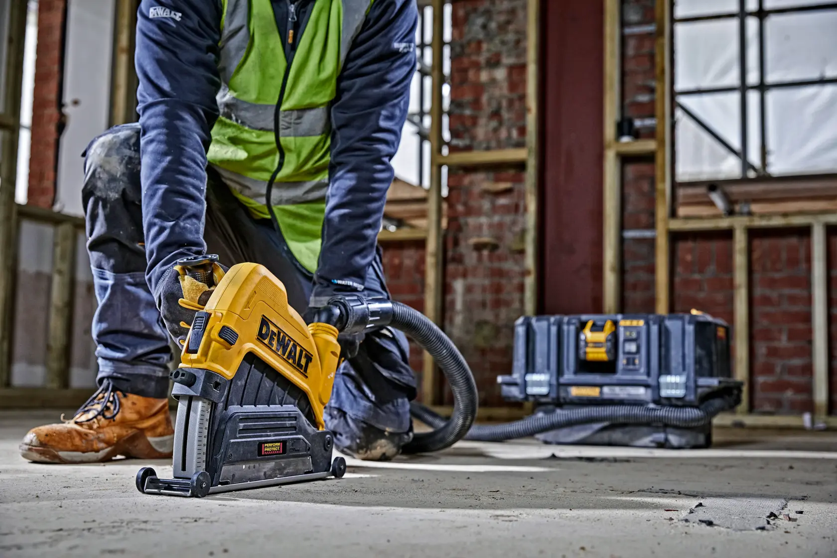 Person nutzt DEWALT Mauernutfräse auf Betonboden in Baustelle. Werkzeugkoffer im Hintergrund.